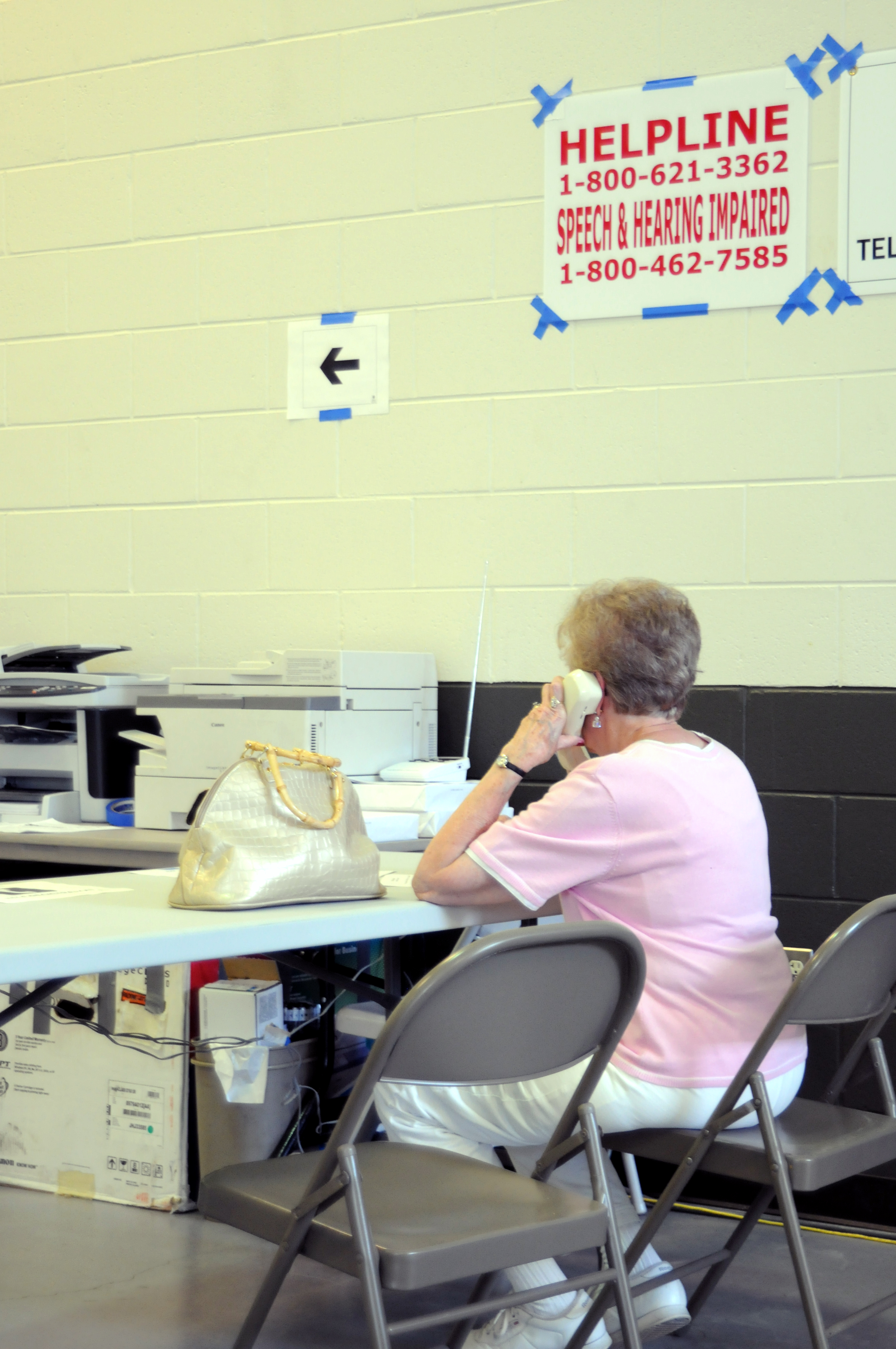Woman on telephone at a folding table beneath a FEMA Helpline sign.