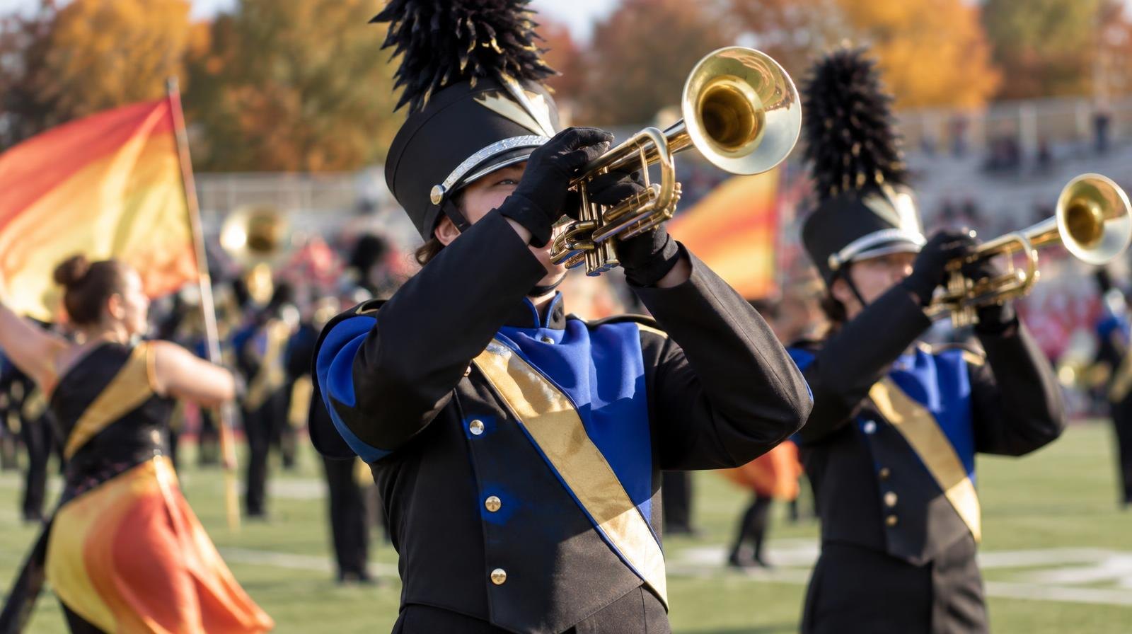 Marching band in colorful uniforms performing on a football field on a sunny day.