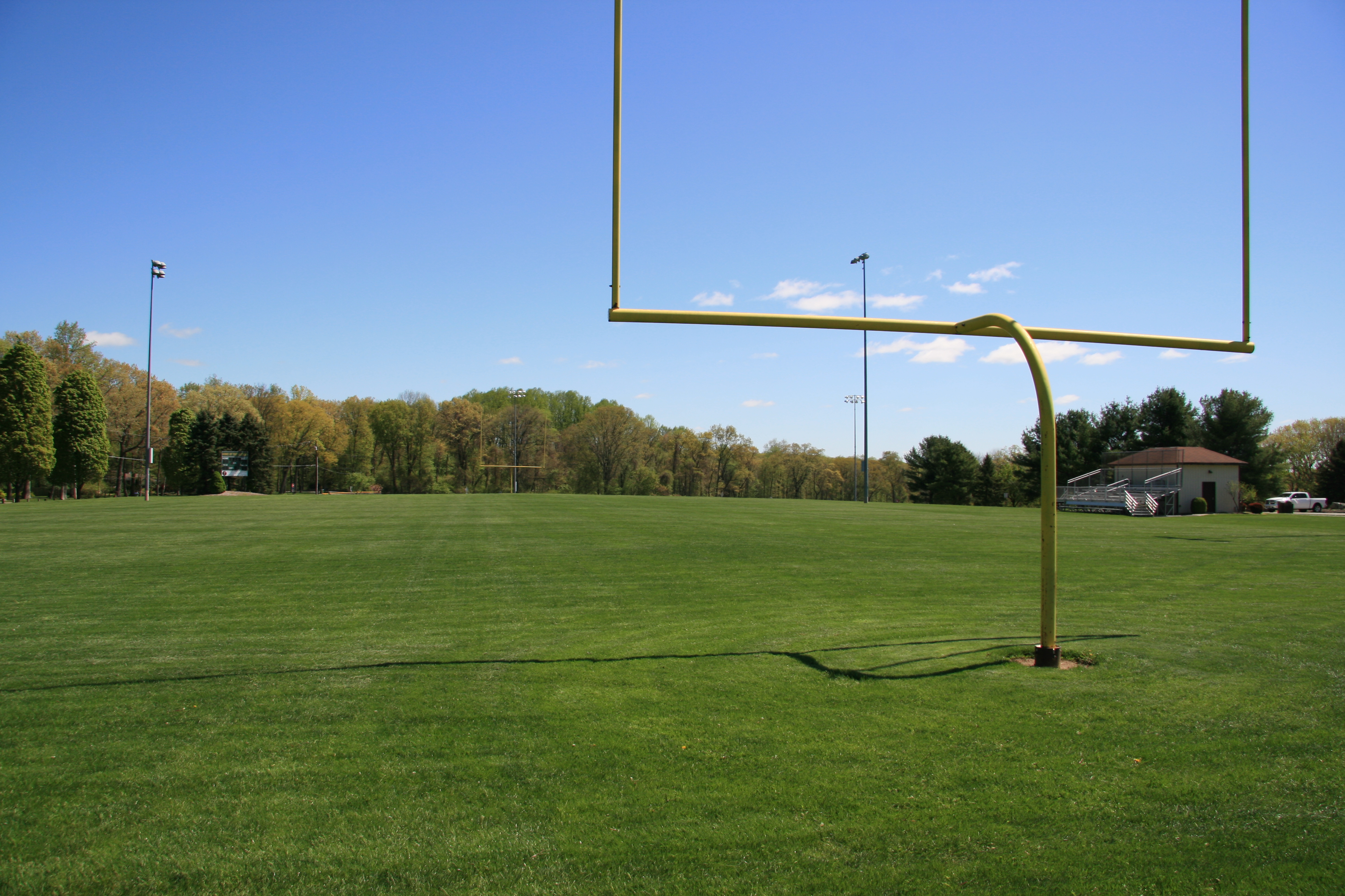 Green grass football field with yellow goalposts and light poles under a blue sky.