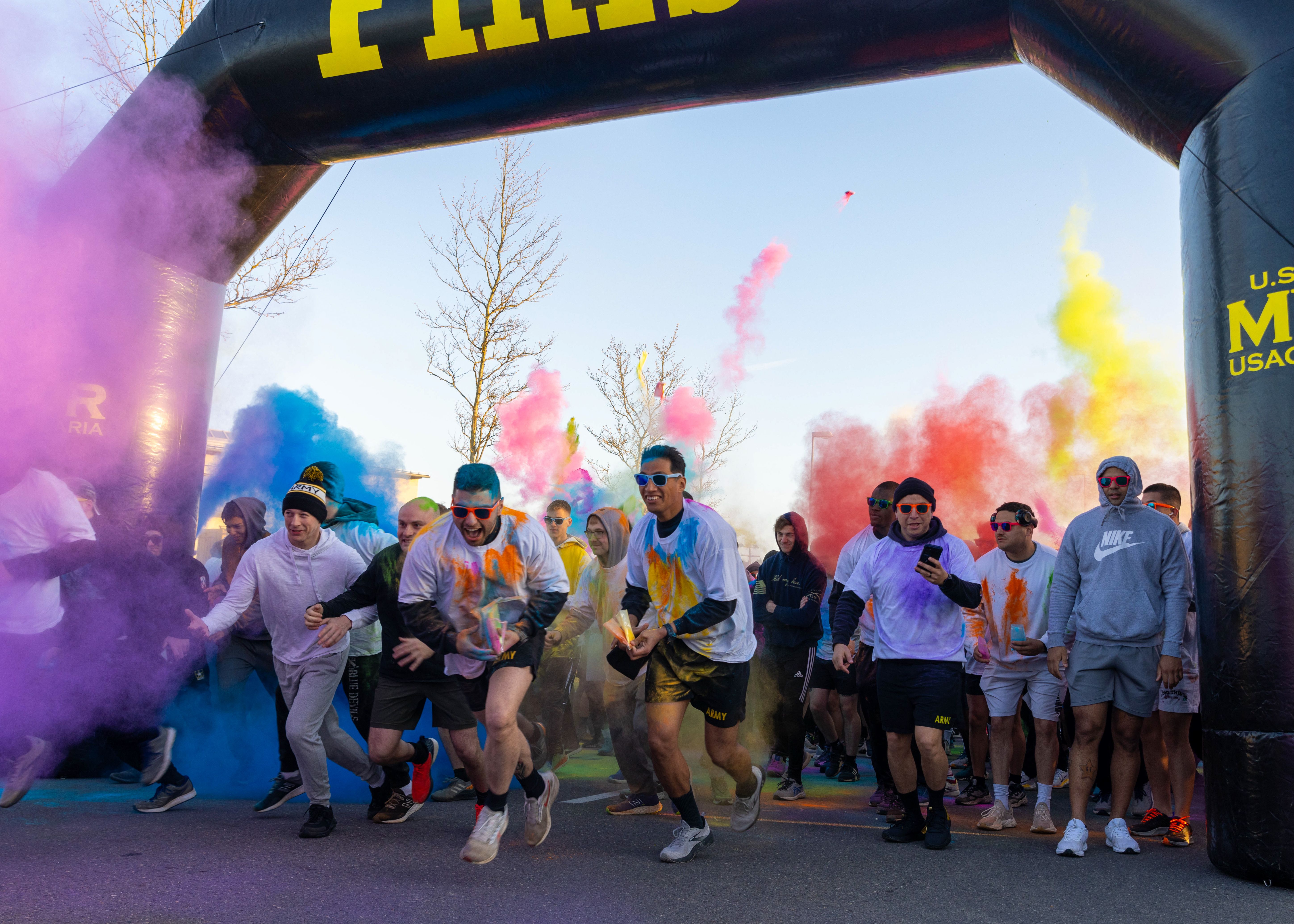 Runners burst through colorful powder explosions under an inflatable arch at a 5K race start.
