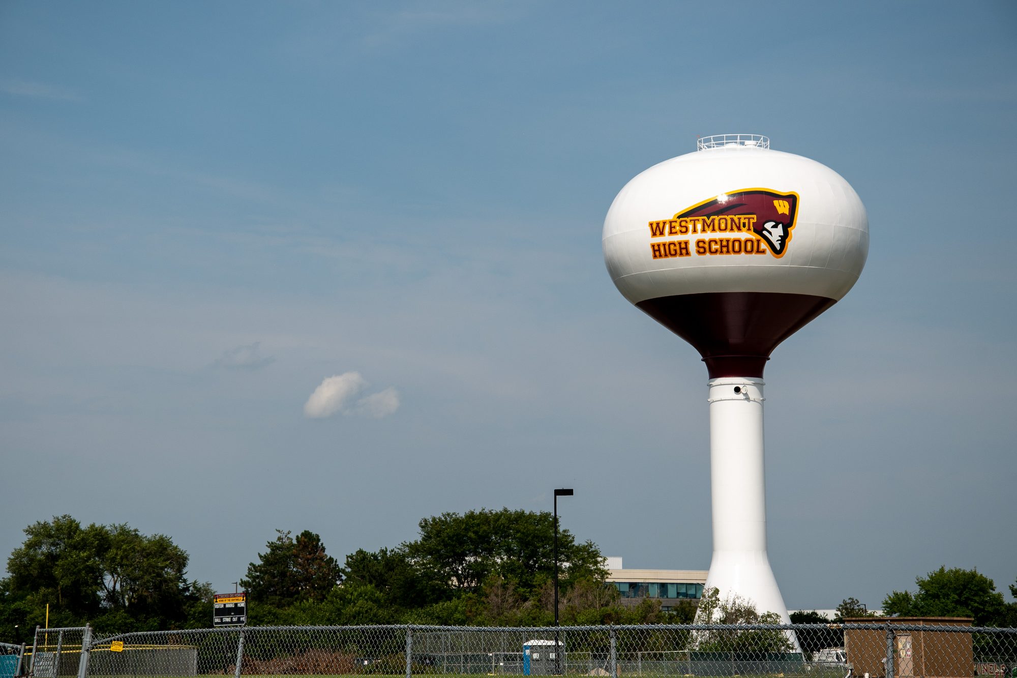 White water tower bearing a high school name and logo against a partly cloudy sky.