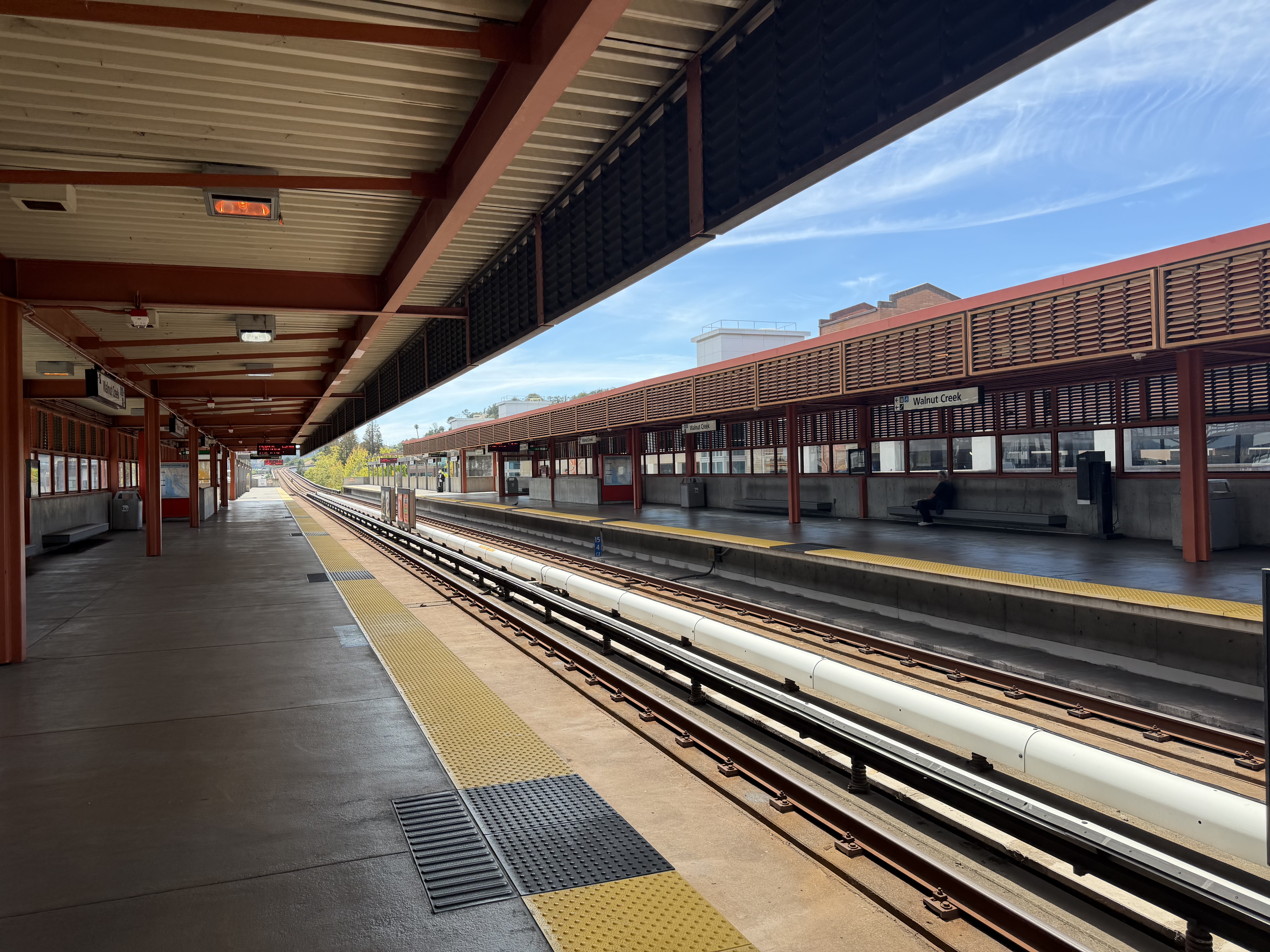 Empty covered BART station platforms with yellow safety strips and dual rail tracks.