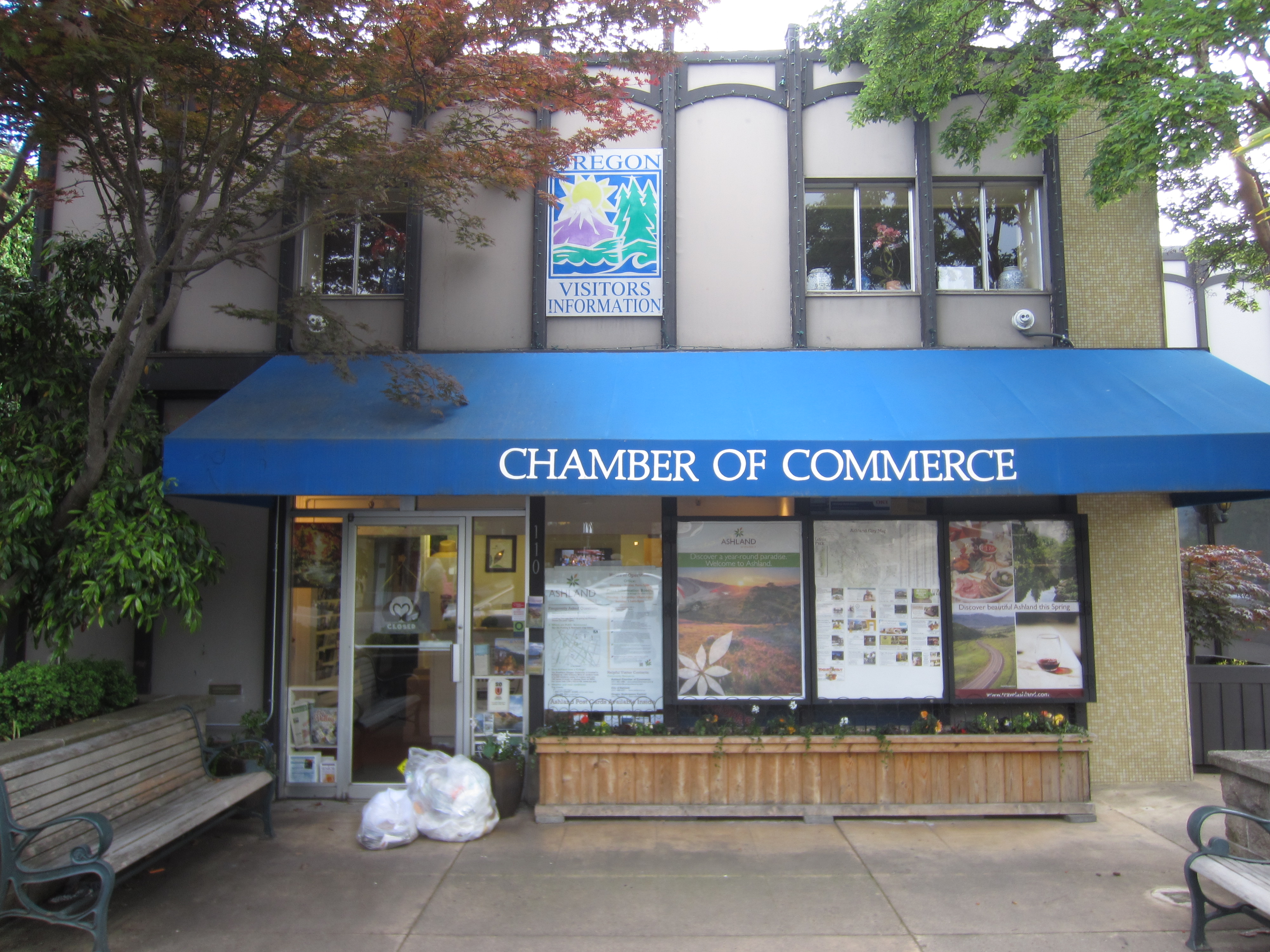 Exterior of a chamber of commerce building with a blue awning and sidewalk benches.