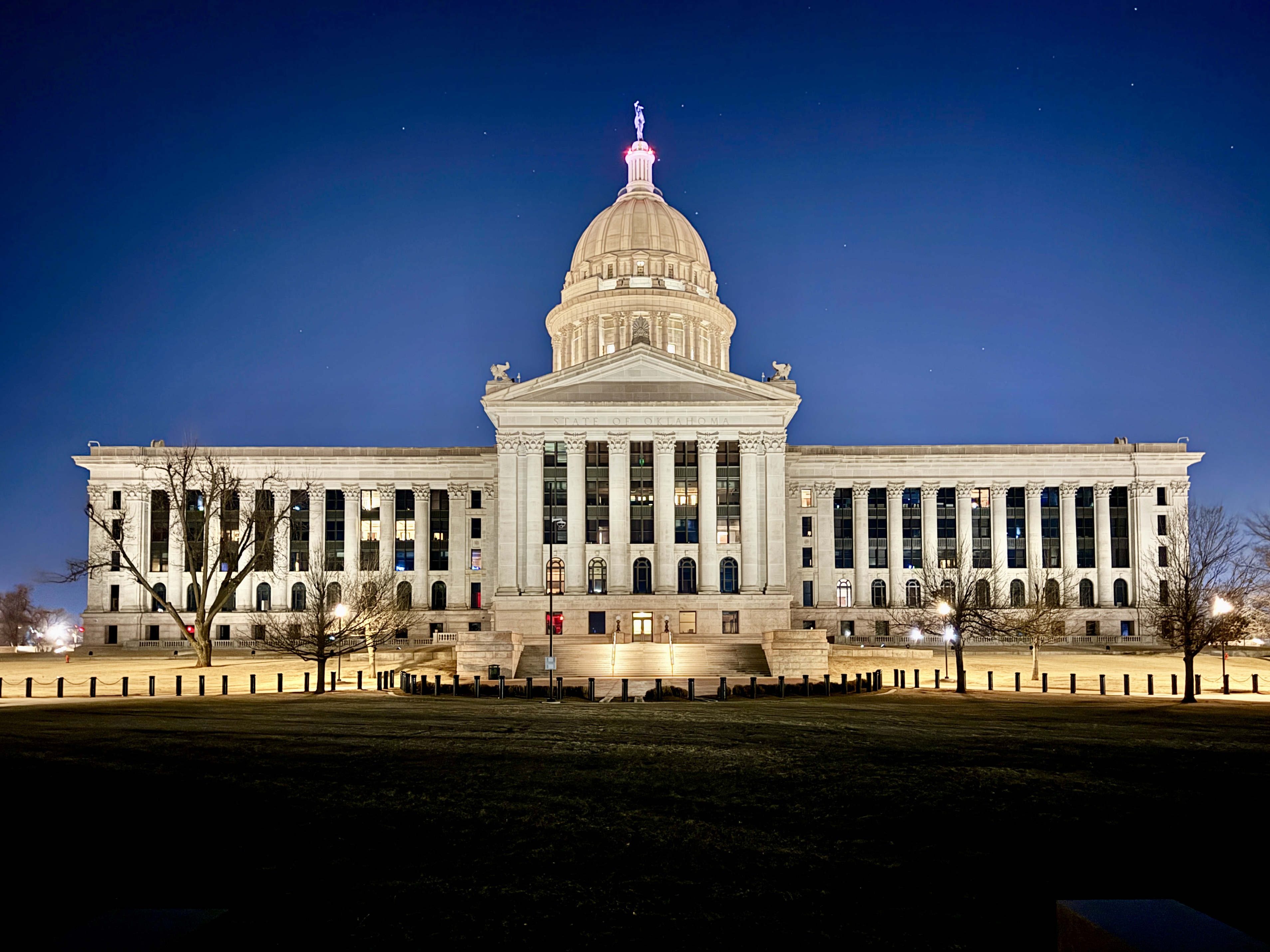 Oklahoma State Capitol building illuminated at night, dome and columns visible.