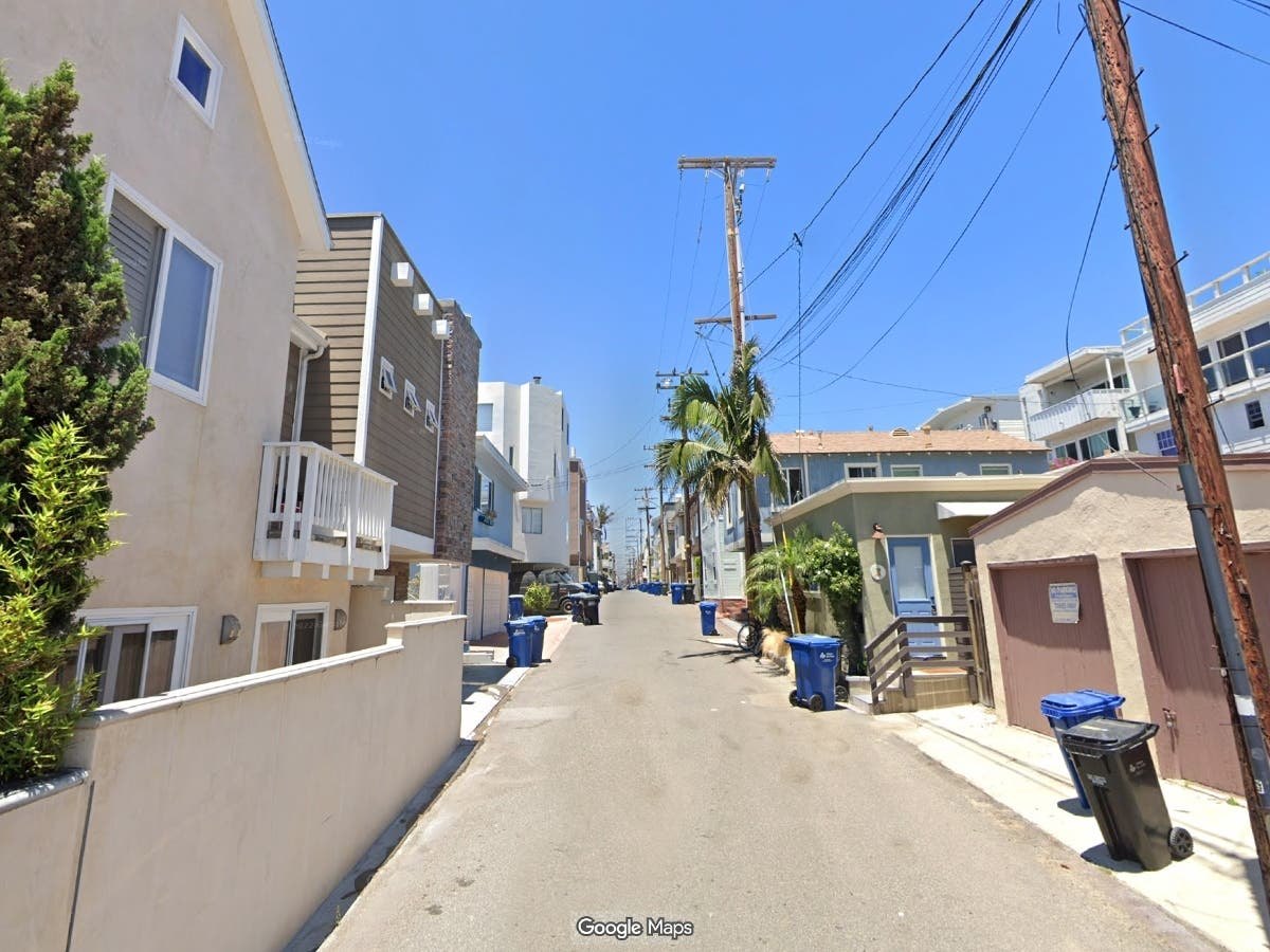 Narrow residential street lined with multi-story homes, utility poles, and overhead power lines.
