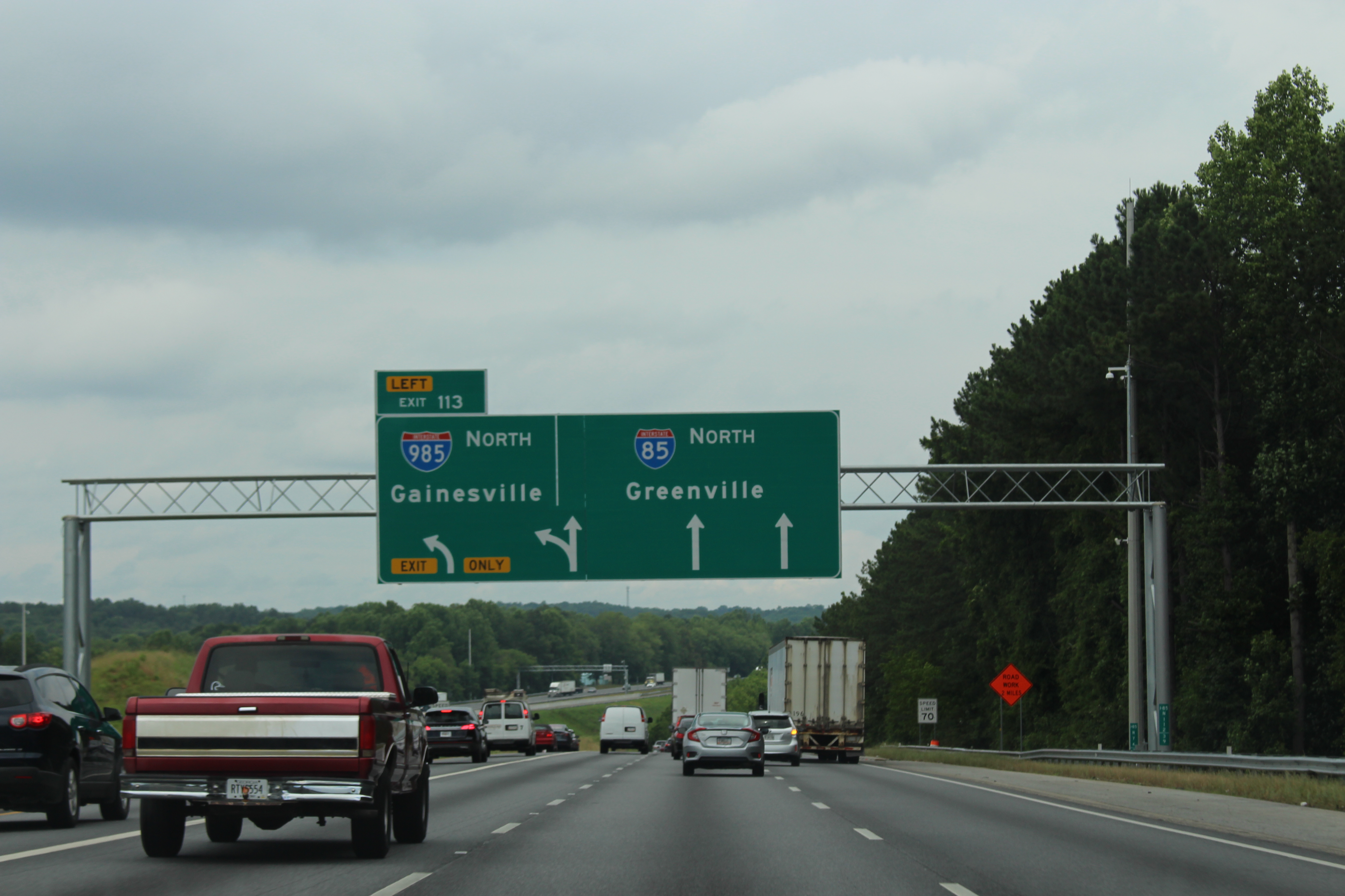 Multi-lane northbound Interstate 85 with green overhead signs under an overcast sky.