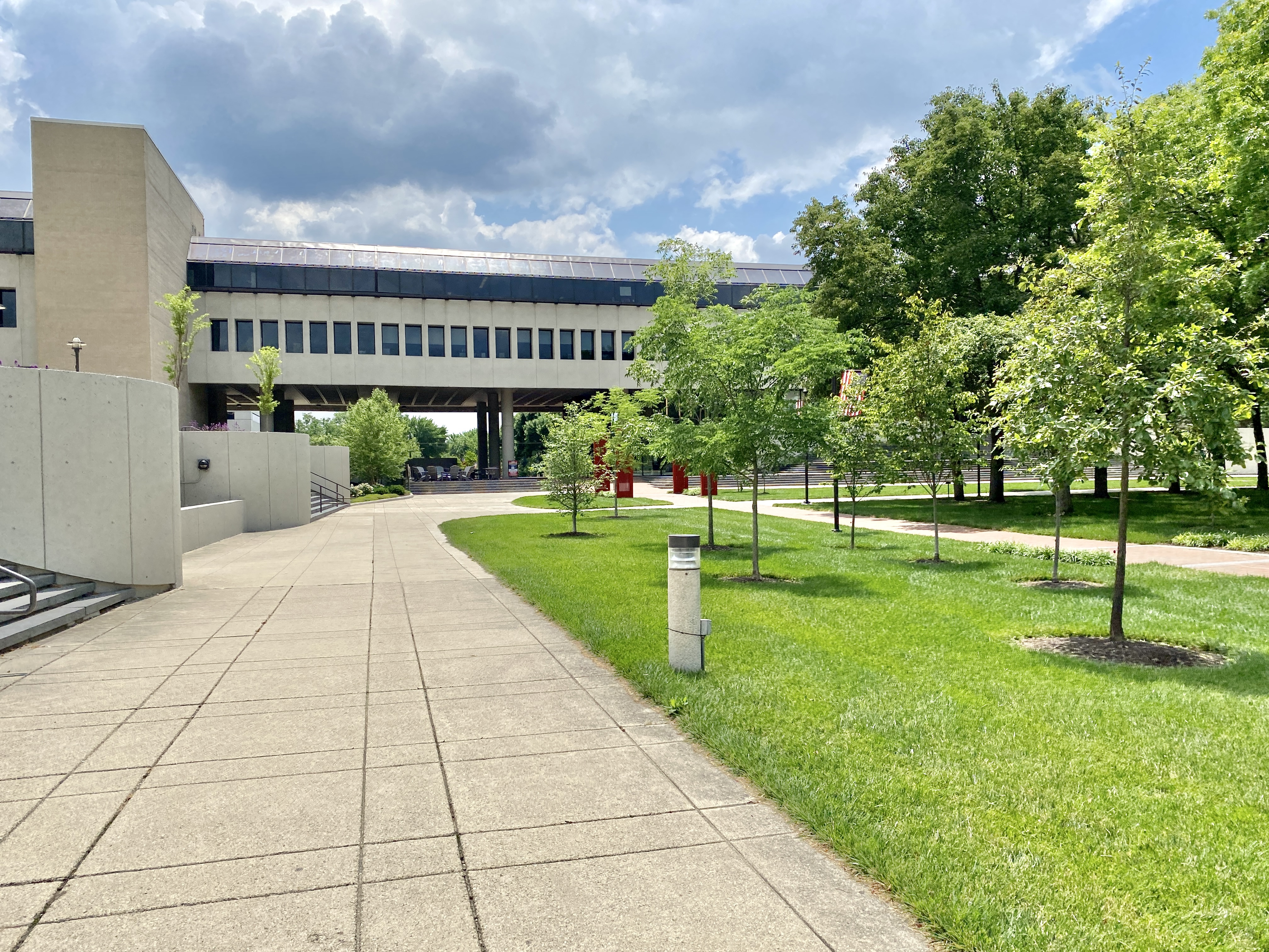 Brutalist concrete college campus buildings with a curved pedestrian walkway and green lawn.