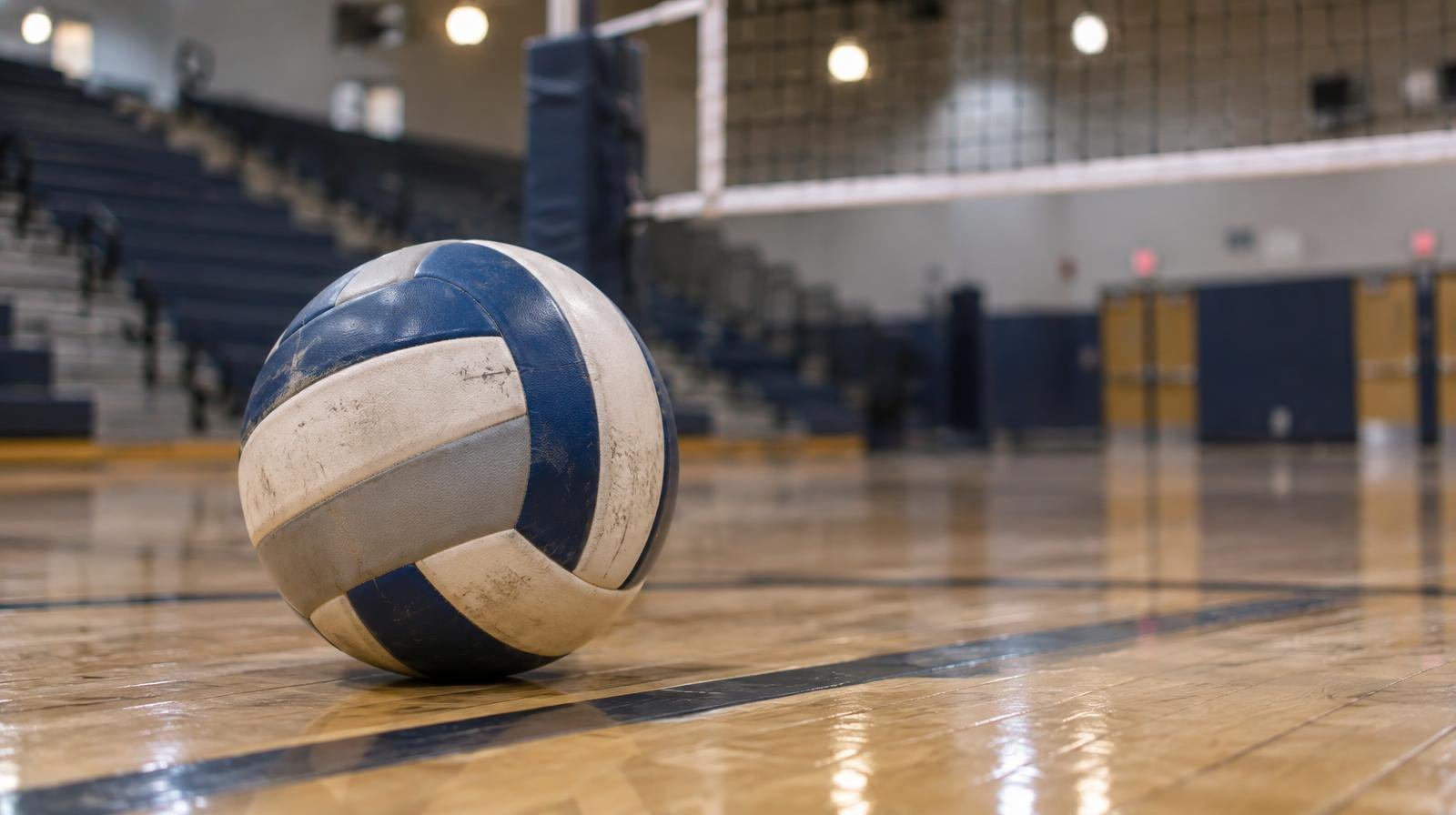 A volleyball resting on a hardwood gymnasium floor near the net.