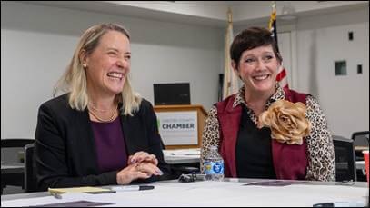 Two women in business attire laugh together at a table during a meeting.