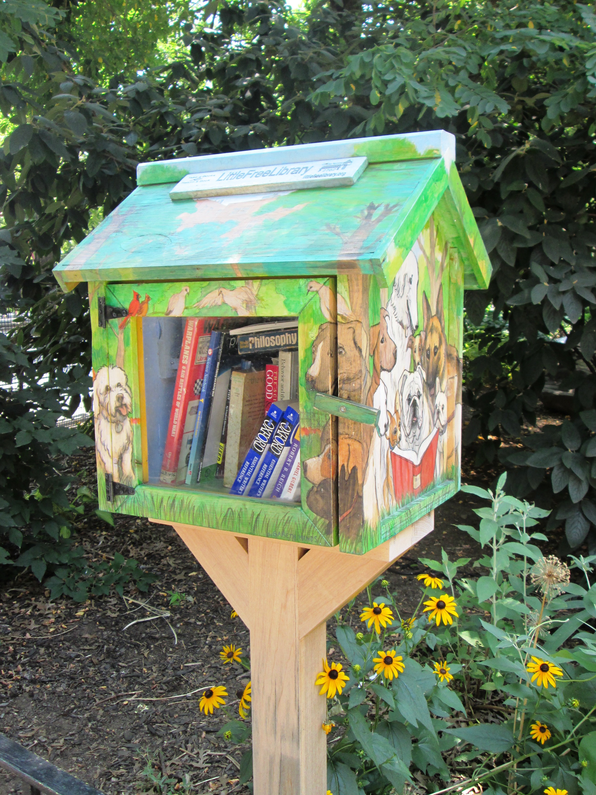 Painted wooden Little Free Library box on a post, open door revealing books inside.