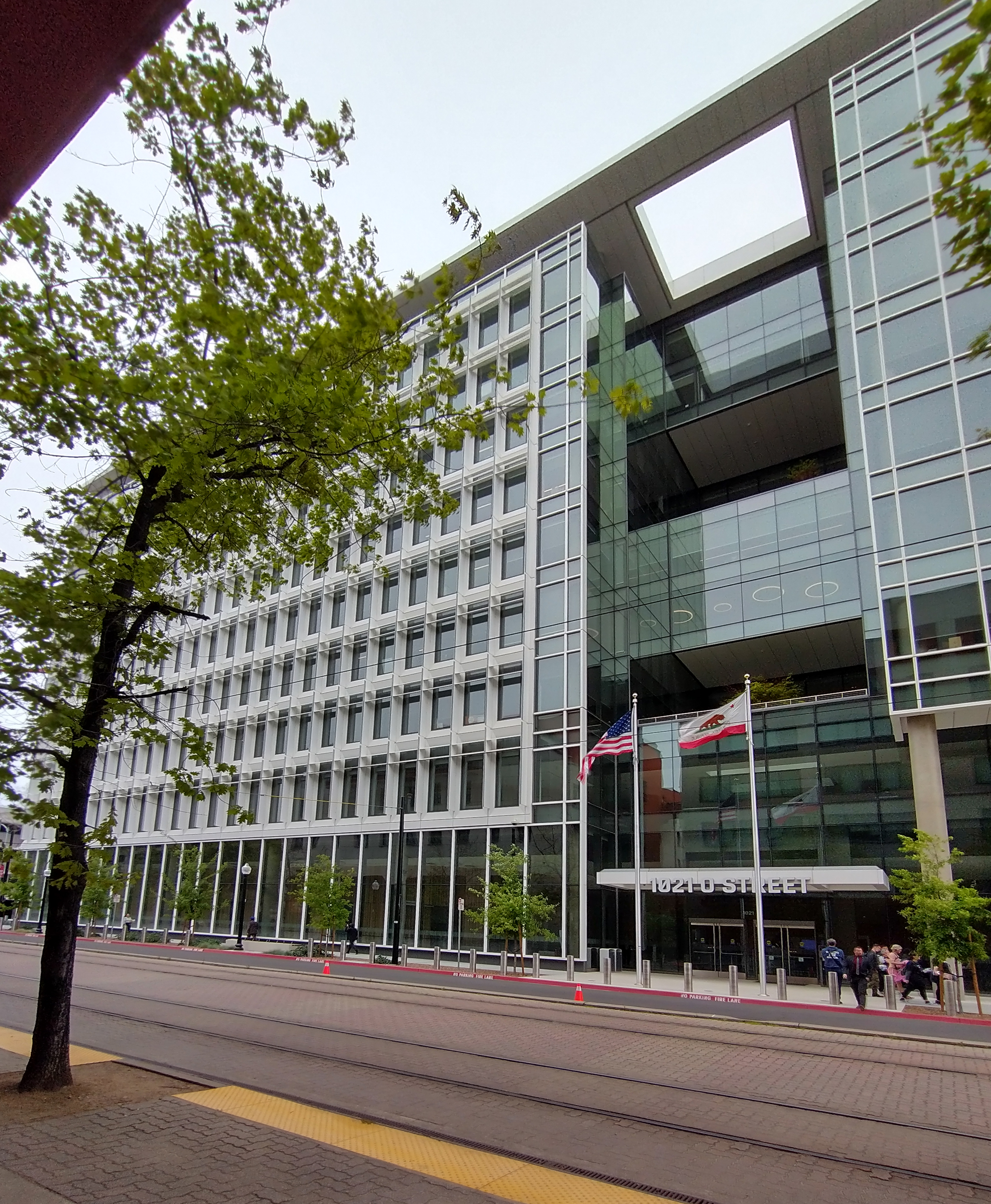 Modern multi-story government office building with American and California flags outside.