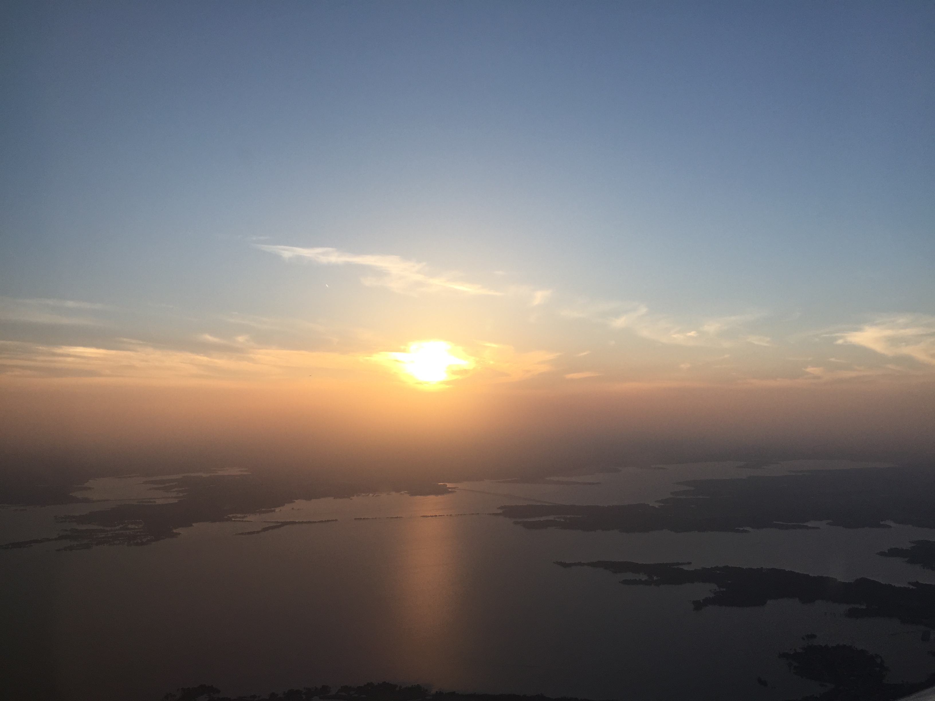 Aerial view of a large lake at sunset with scattered islands and hazy sky.