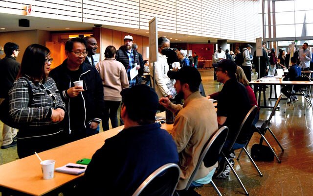 People gathered at tables in a modern indoor atrium during a community event.