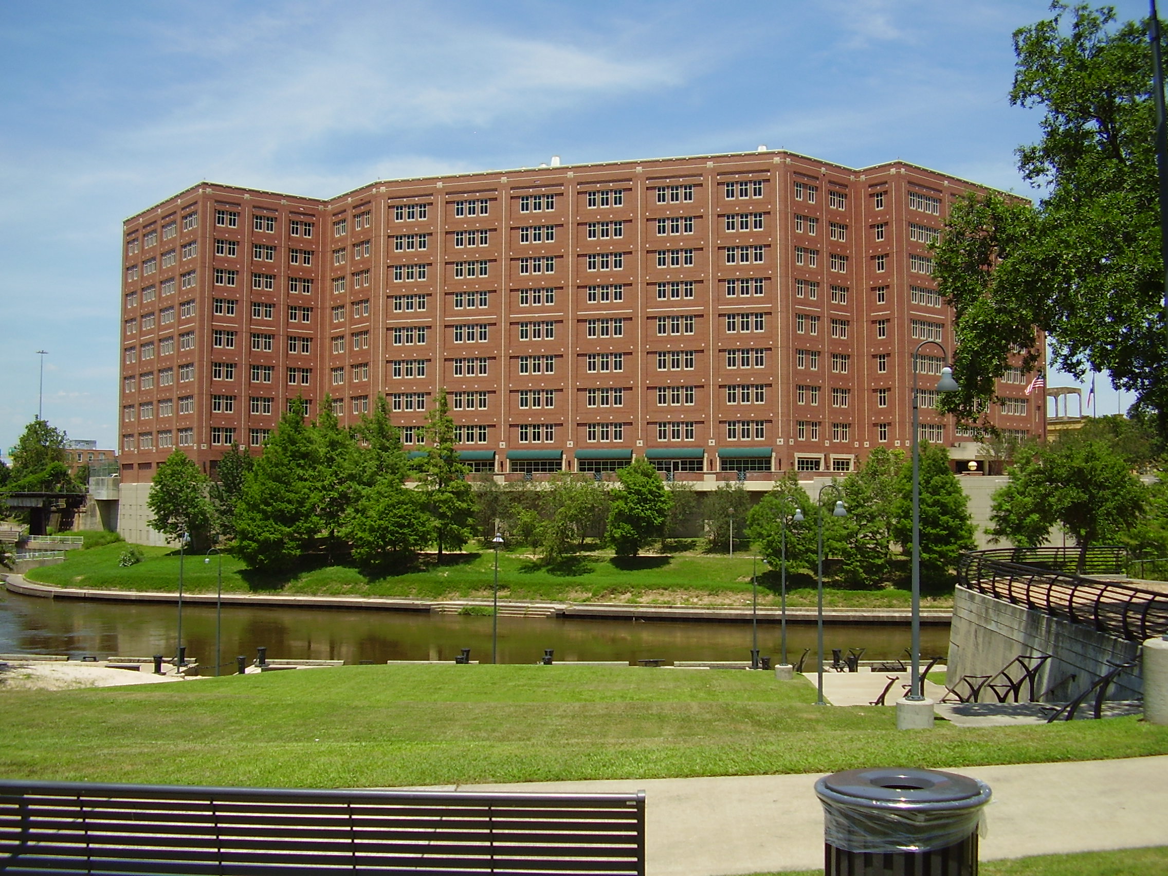 Multi-story red brick jail building beside a canal with green lawn and trees in the foreground.