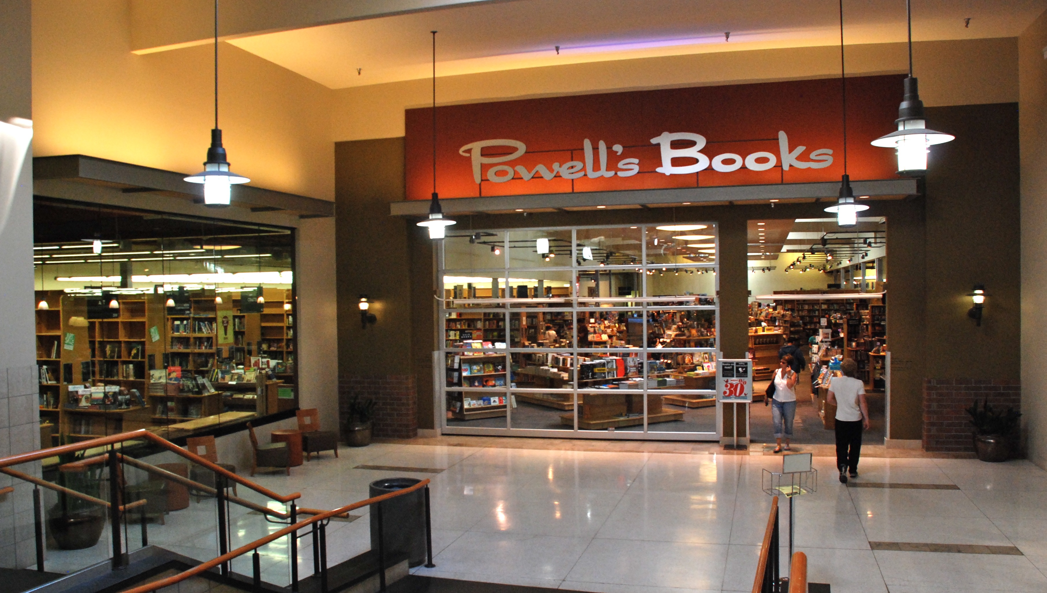 Mall corridor entrance to a bookstore with an orange Powell's Books sign above the doorway.