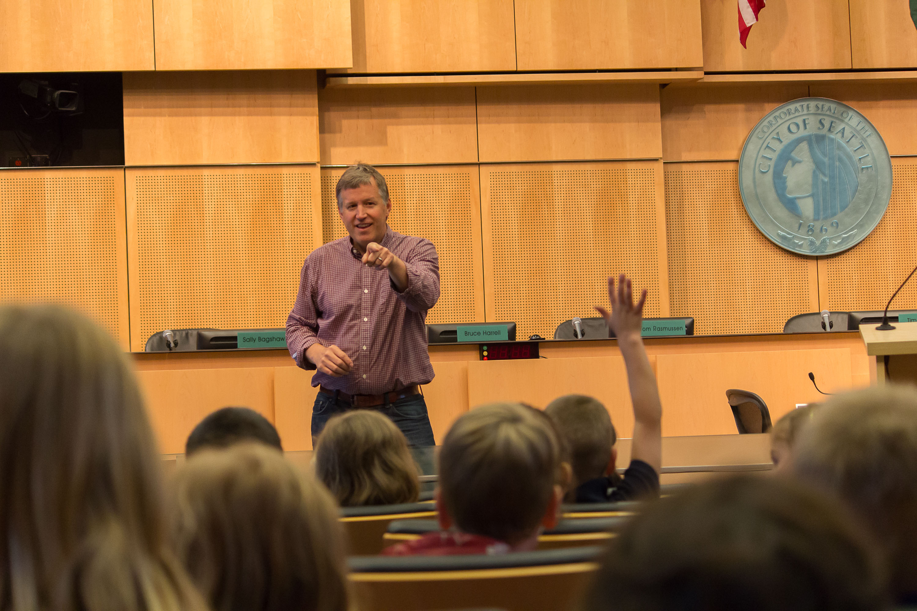 Council chamber interior with raised dais, name placards, and City of Seattle seal on wall.