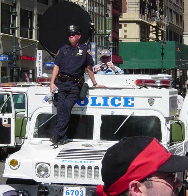 Large acoustic device dish mounted on top of a white police Humvee on a city street.