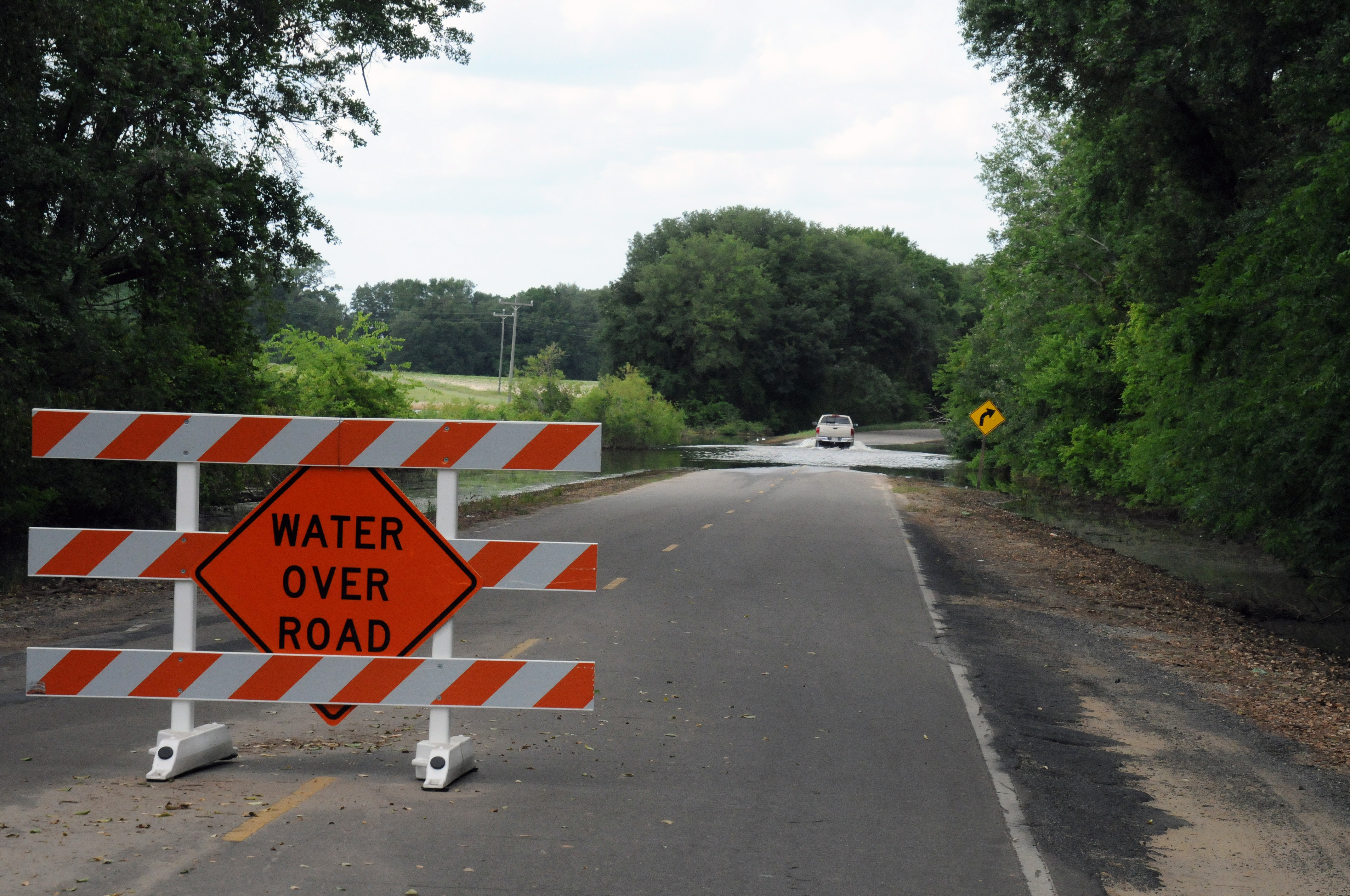 Orange and white barricade with Water Over Road sign blocking a flooded road.