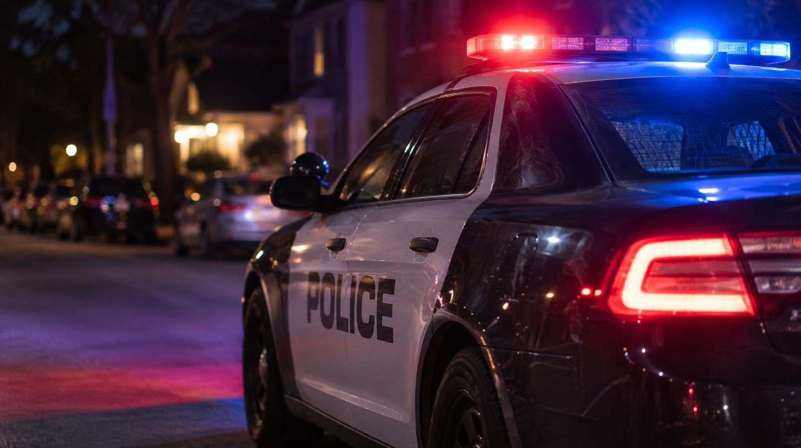 Police patrol car with red and blue emergency lights on a dark residential street.