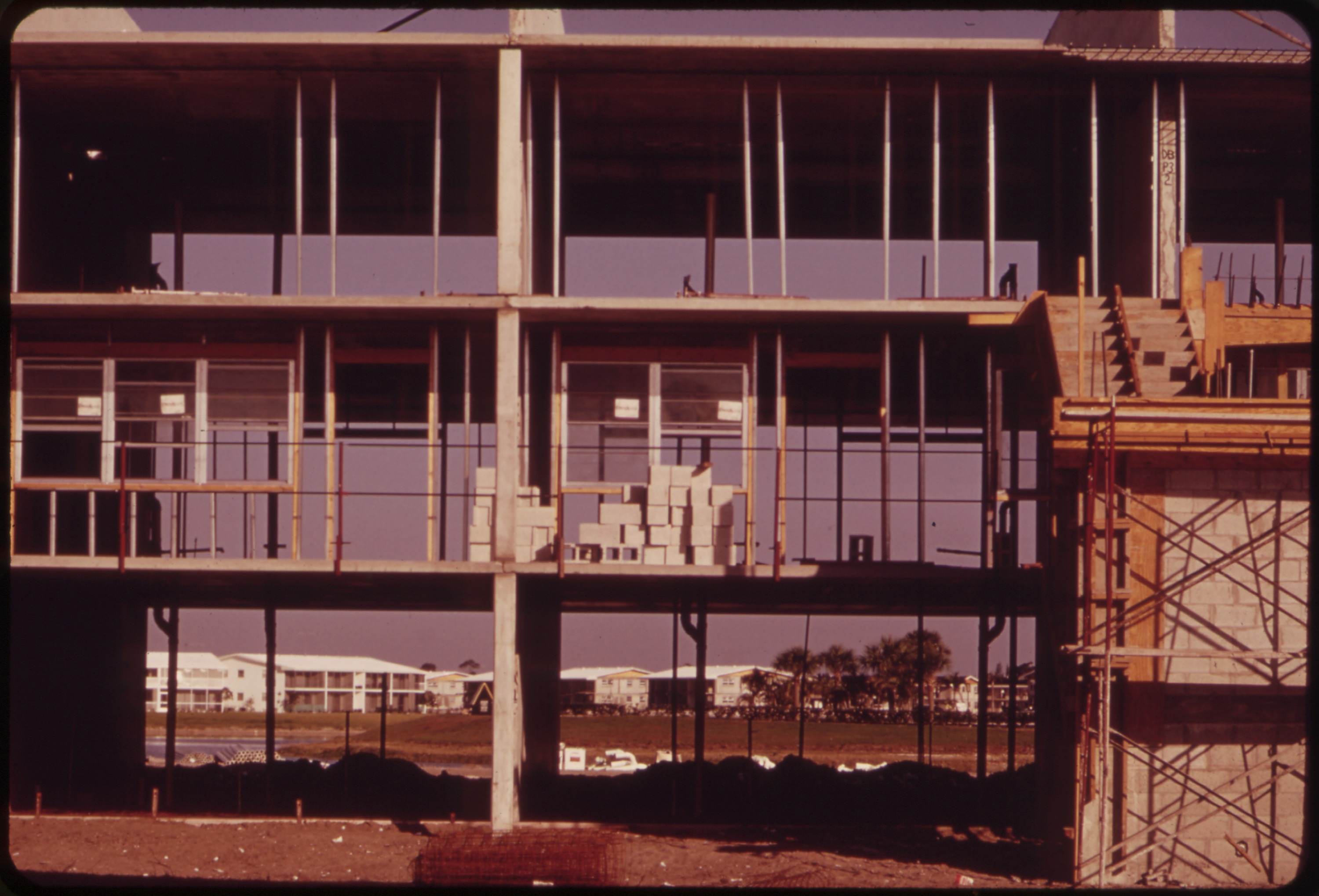 A multi-story concrete apartment building under construction with scaffolding and stacked materials on upper floors.