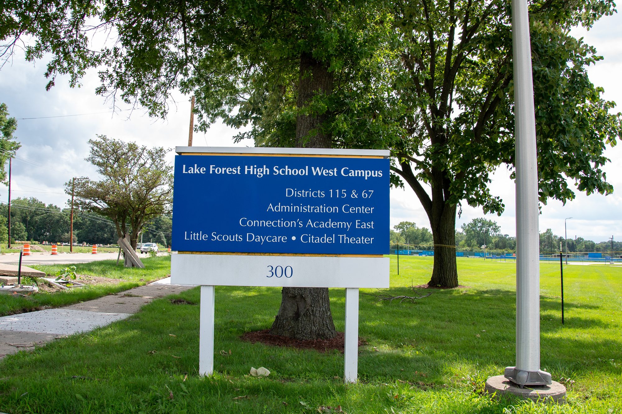 Blue institutional sign for a high school west campus on a landscaped lawn
