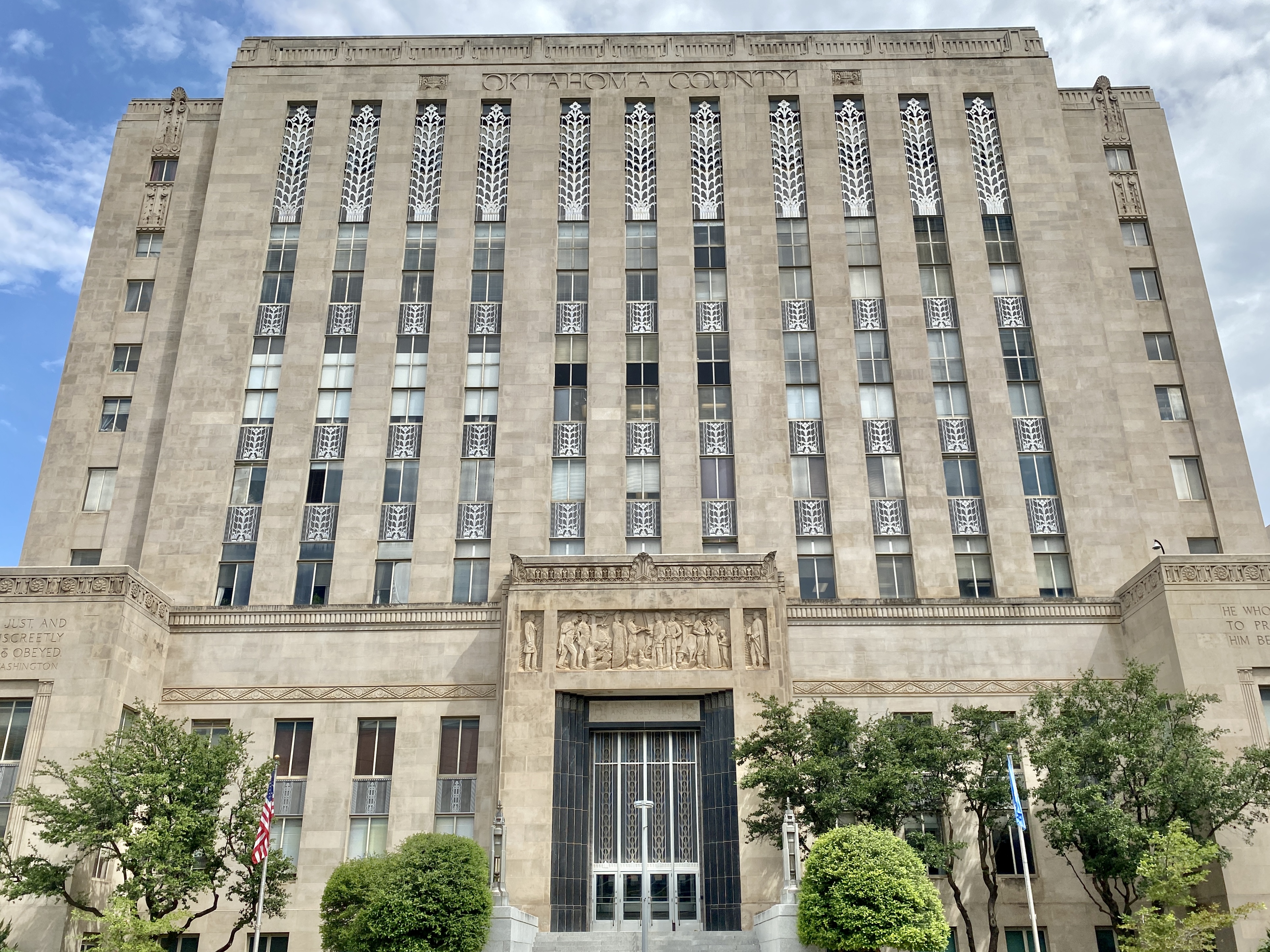 Art Deco government building facade with decorative friezes and an American flag.