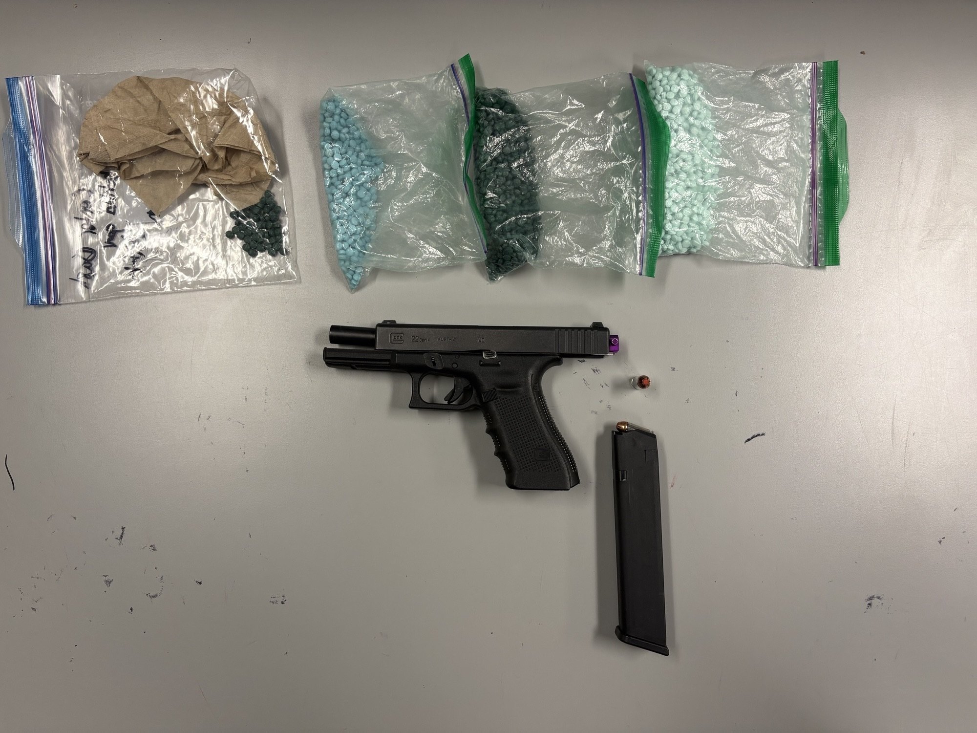 Bags of small blue pills and a black handgun with extended magazine on a gray surface.