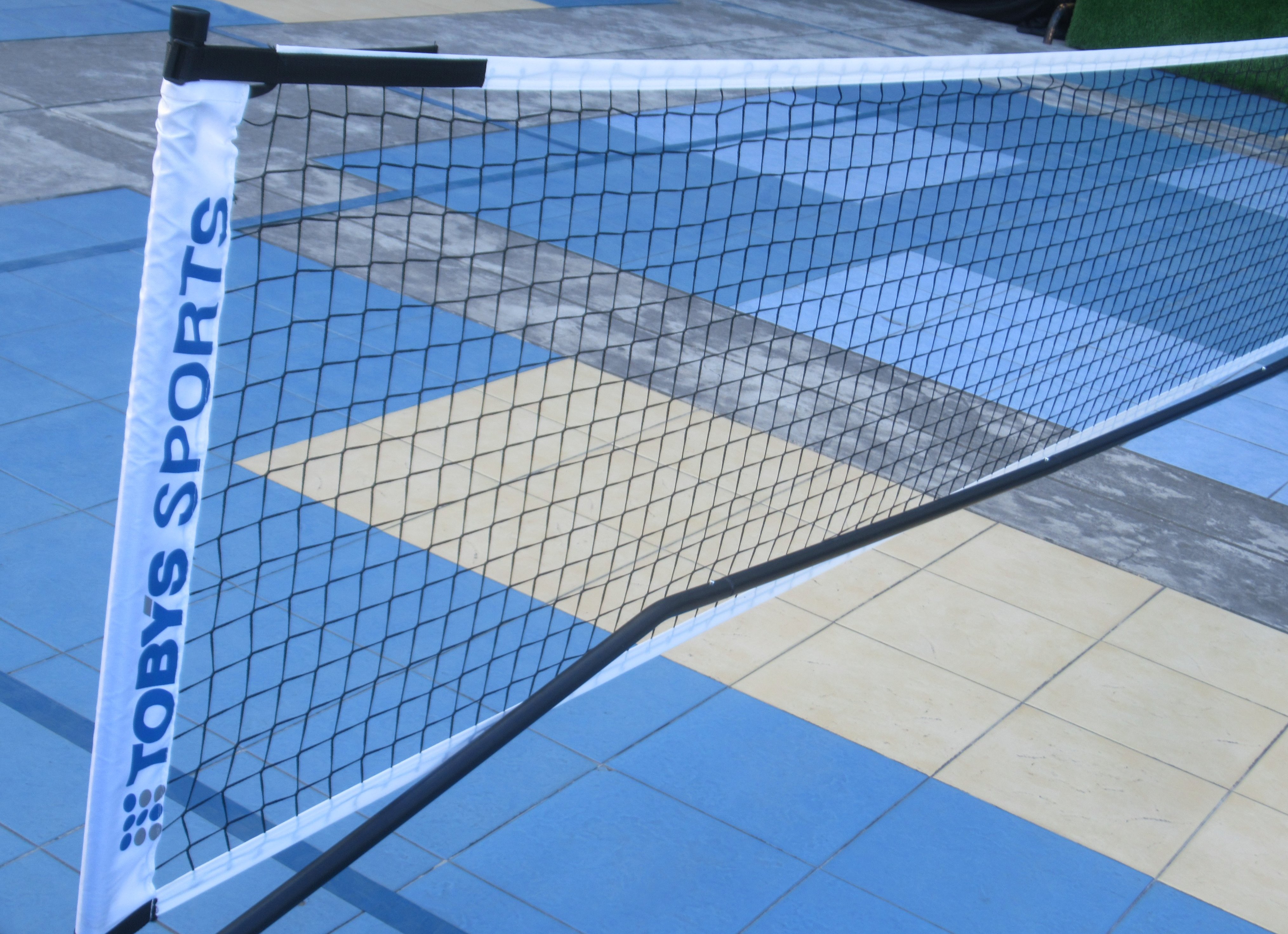 Outdoor blue pickleball court with a net, viewed from court level, showing surface discoloration.