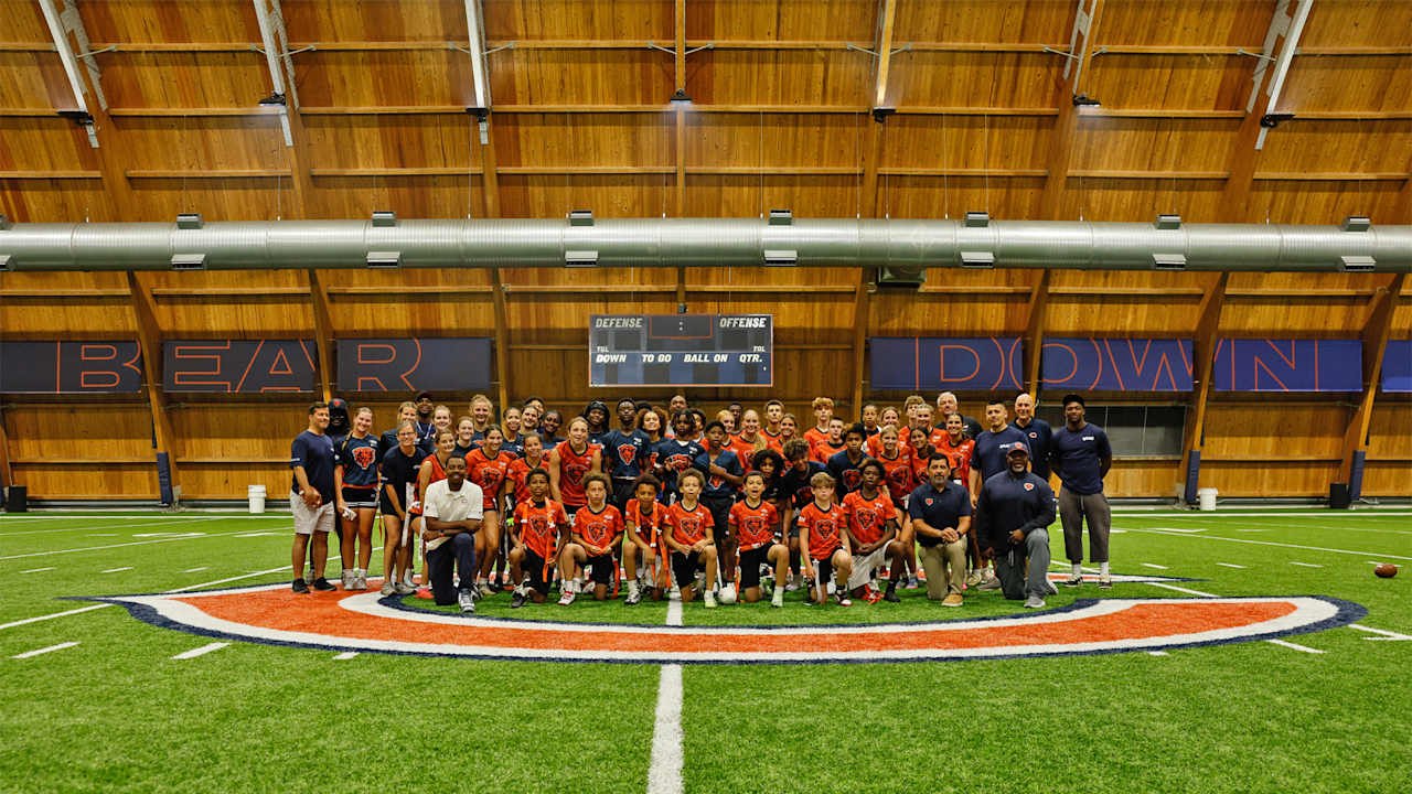 Large group of youth athletes and coaches posing on an indoor turf field with 'Bear Down' on the wall.