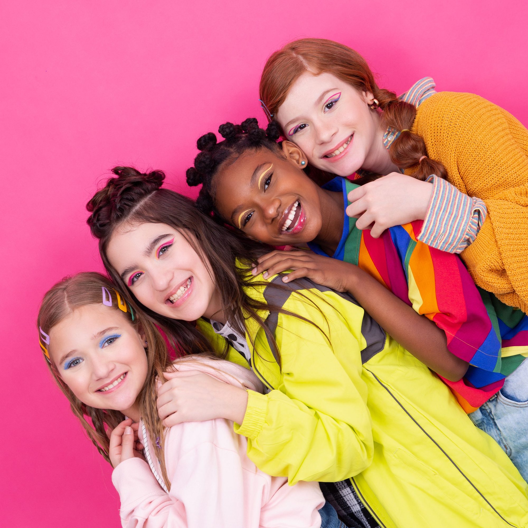Colorful group portrait of teenage girls posing joyfully against a pink background.