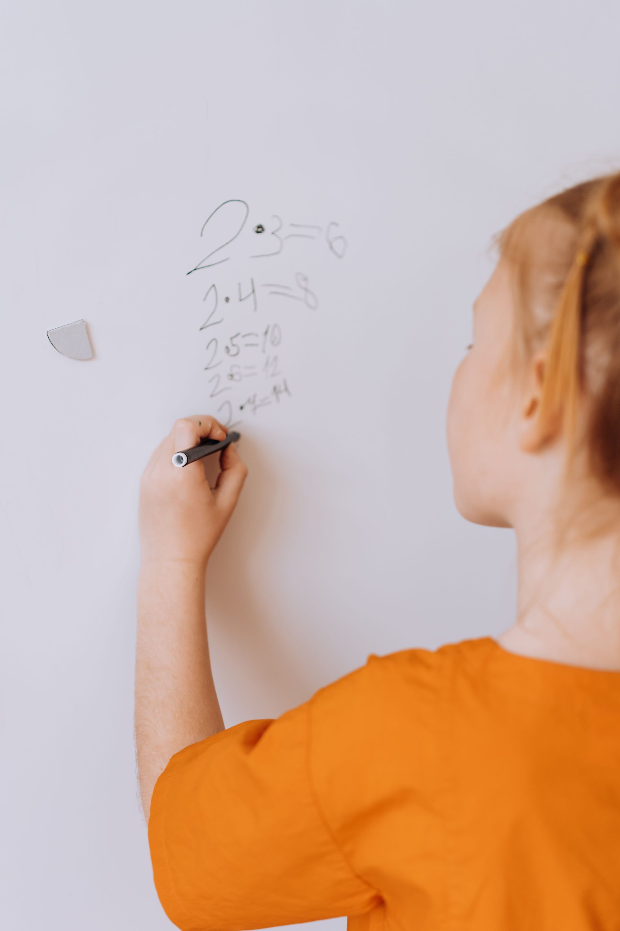 A young girl solving math problems on a whiteboard indoors, showcasing education and learning.