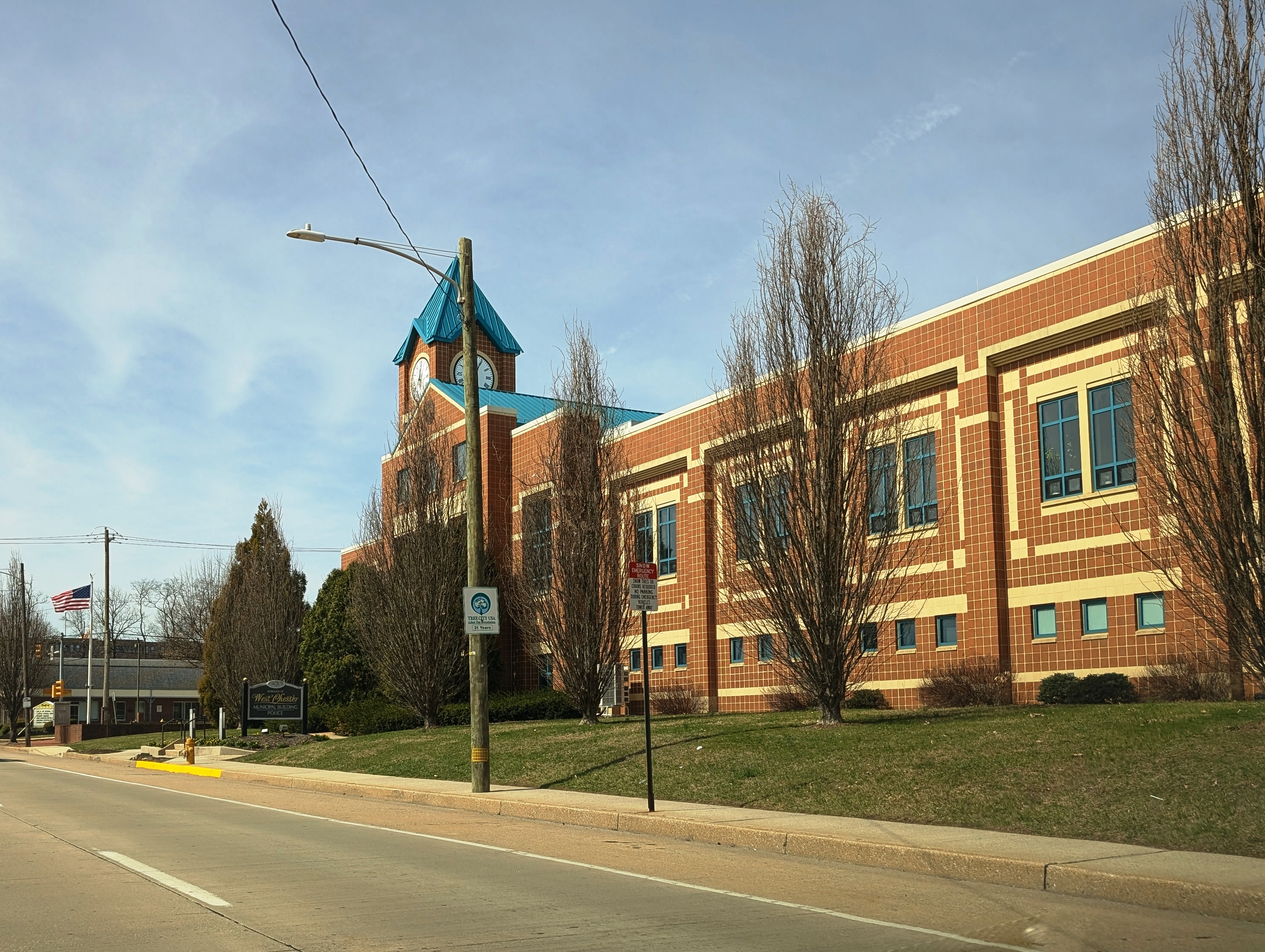 Red brick municipal building with a blue clock tower on a downtown street.