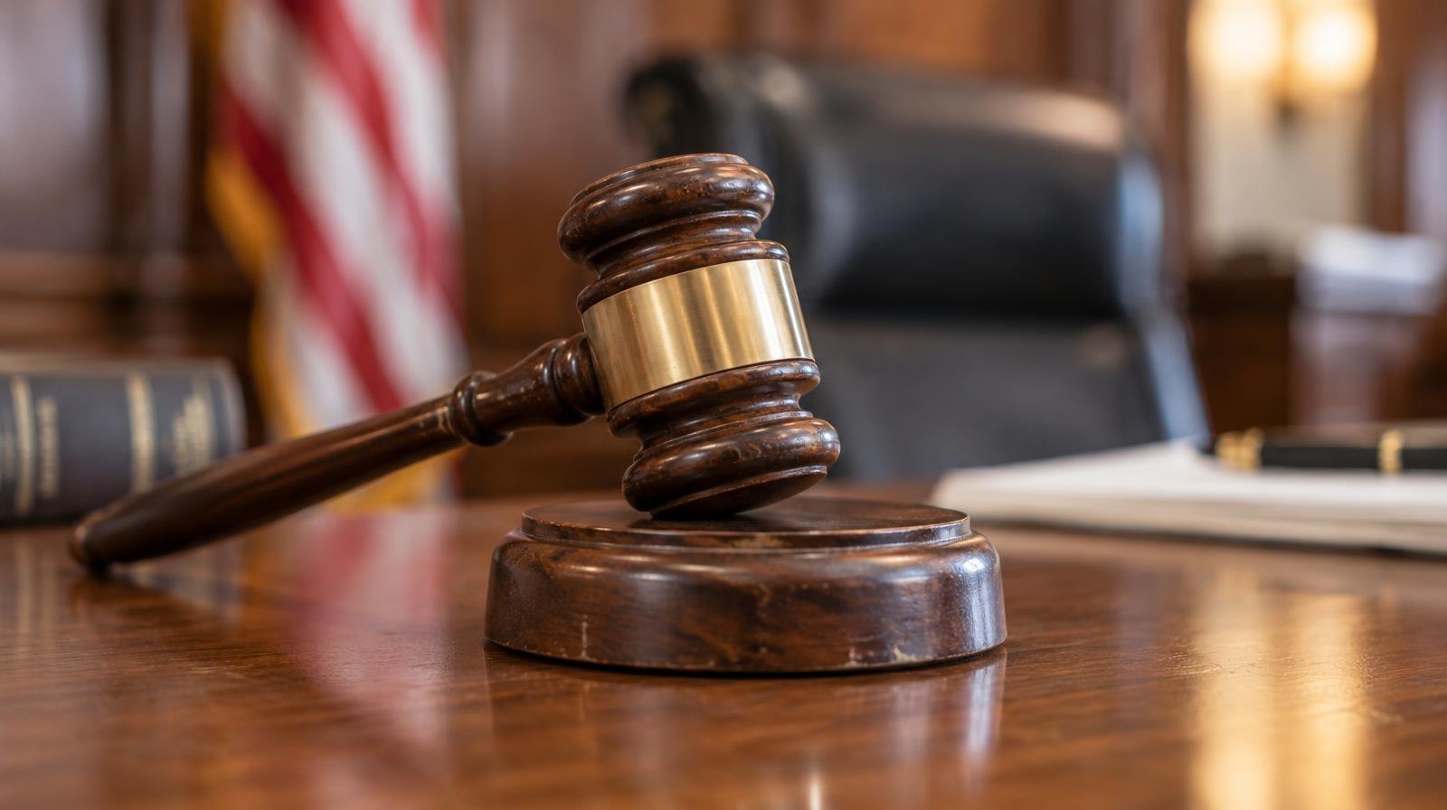 A wooden judge's gavel resting on its sound block on a polished wooden surface.