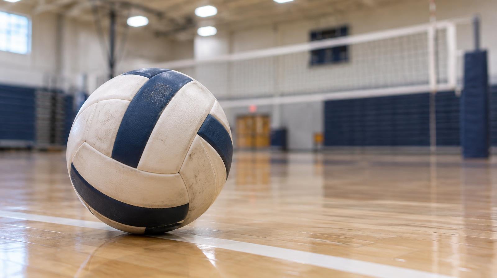 A volleyball resting on a hardwood gym floor beside a white boundary line.