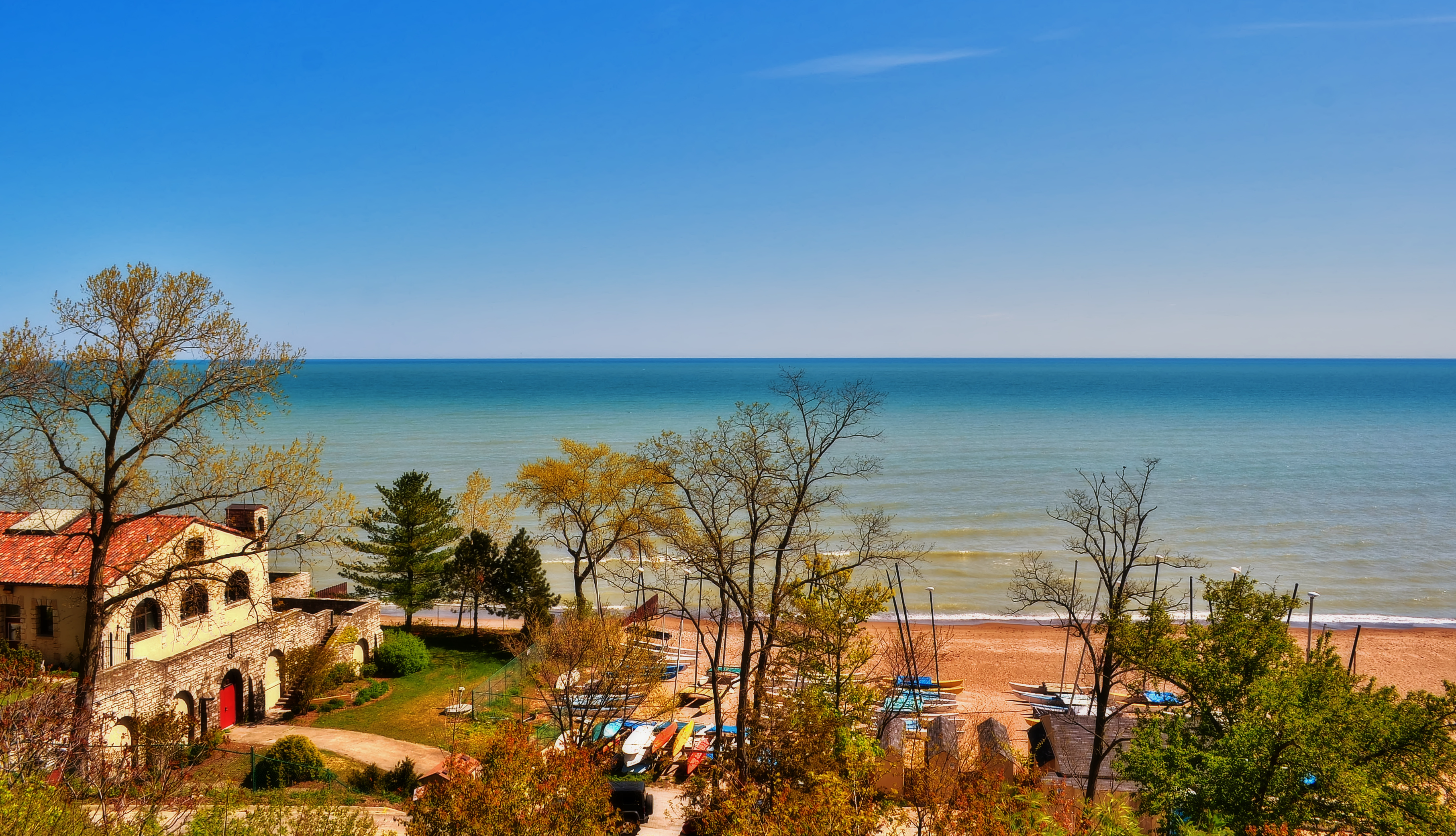 Stone building nestled among trees beside a calm blue lakefront beach.