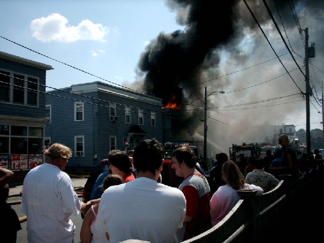 A multi-story building engulfed in flames with thick black smoke rising above.
