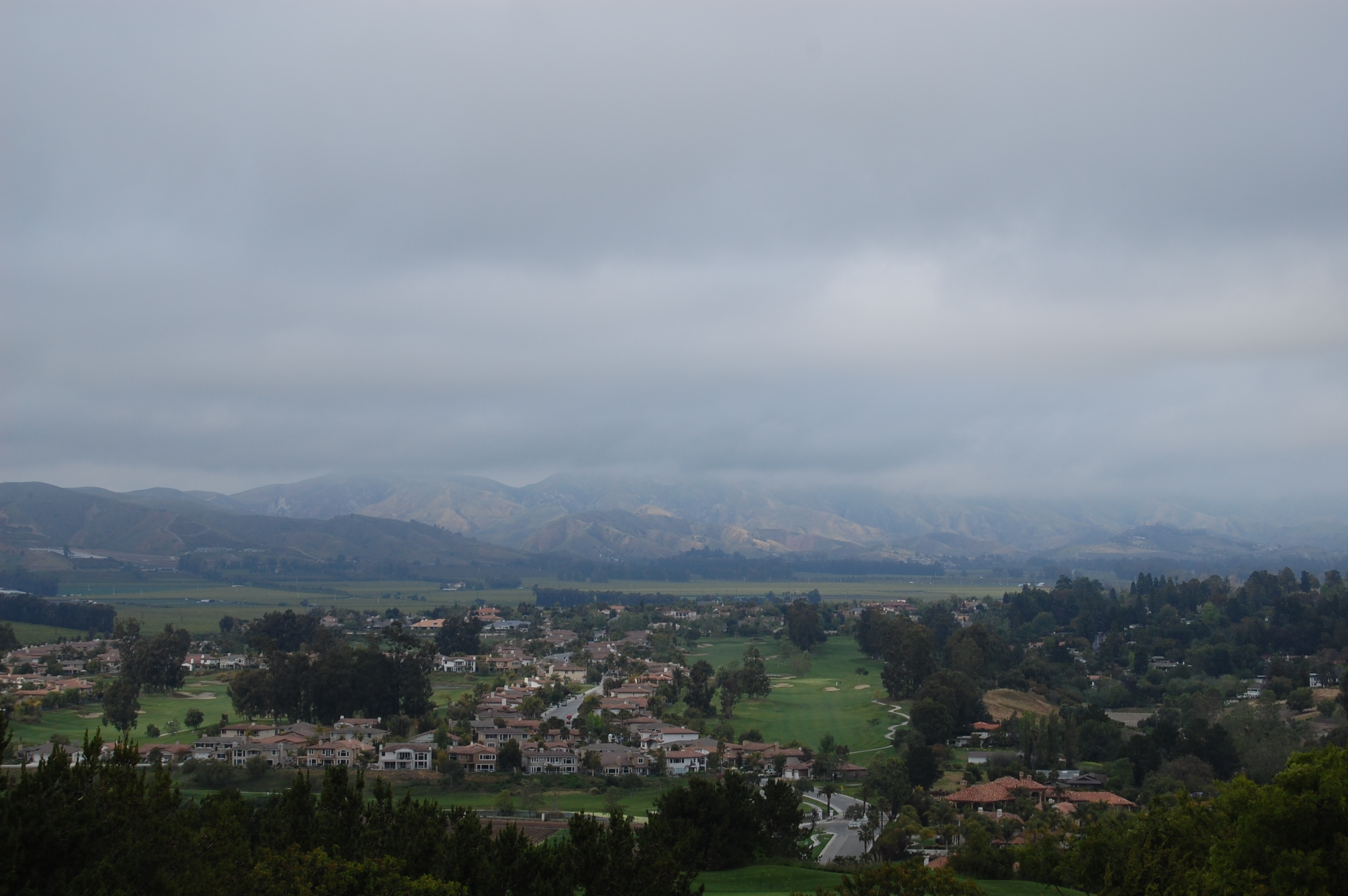 Residential neighborhood in a California city with mountains visible under a cloudy sky.