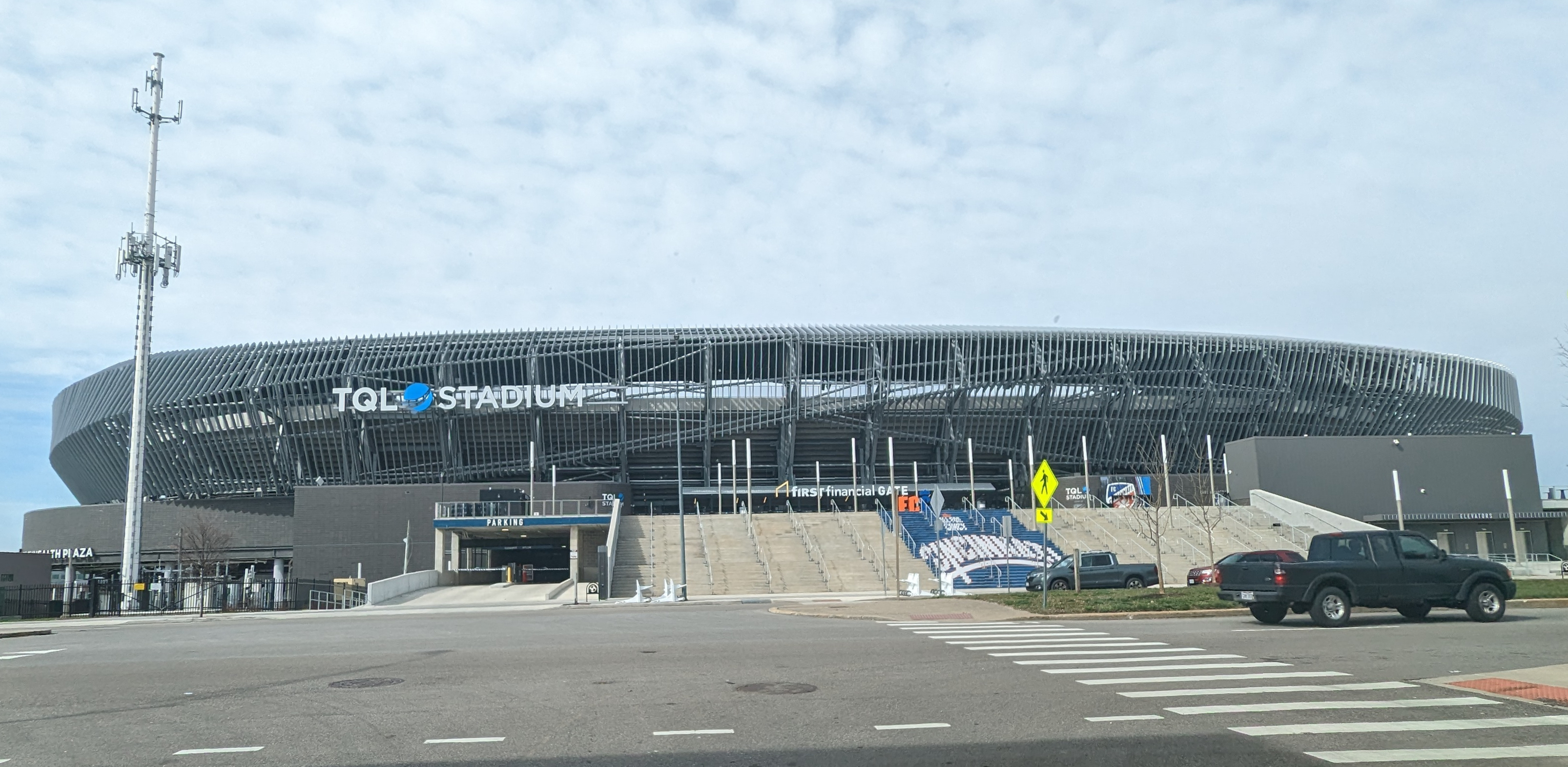 Exterior facade and main entrance of TQL Stadium on a partly cloudy day.