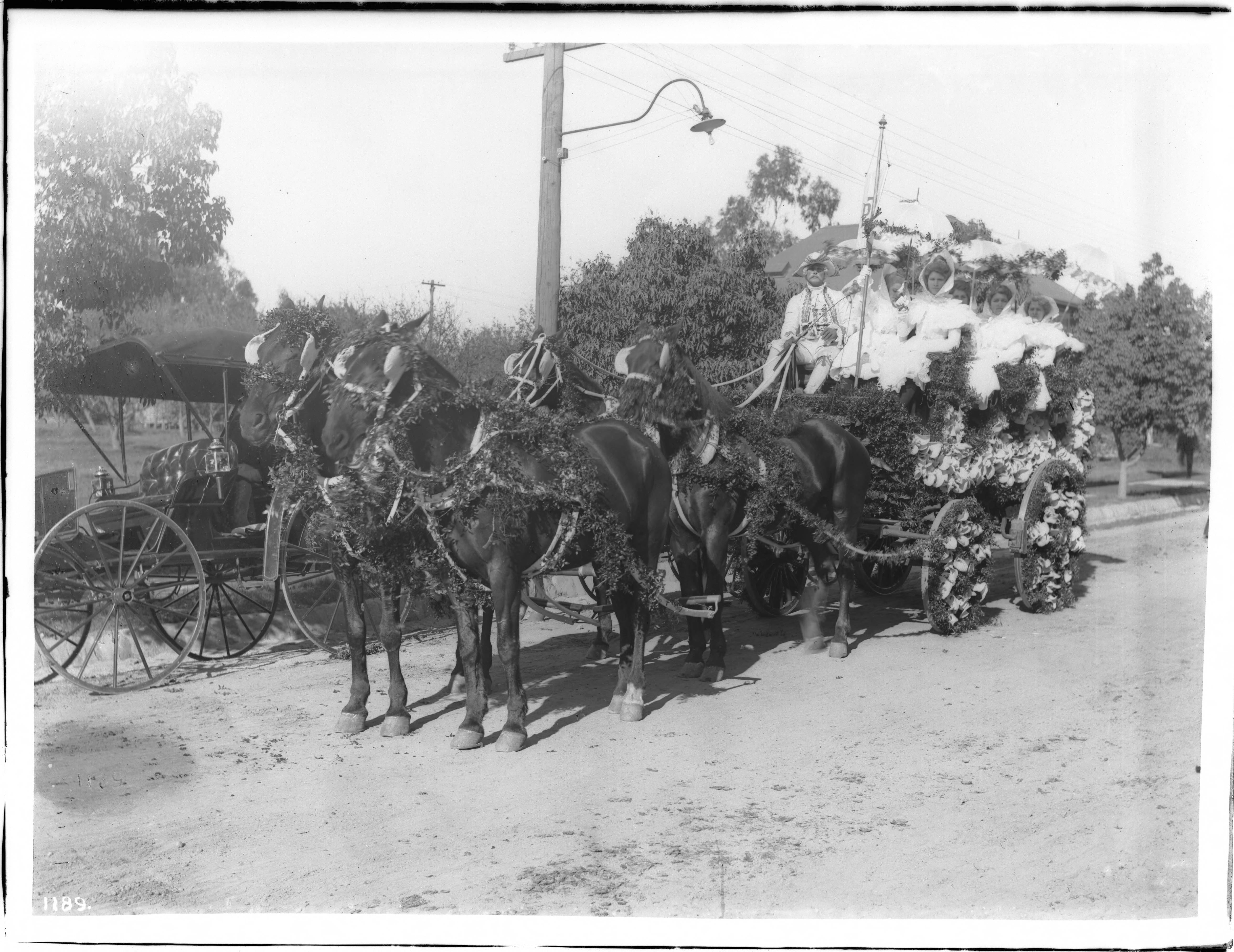 A horse-drawn flower-decorated float carries women with parasols on a historic Pasadena street.