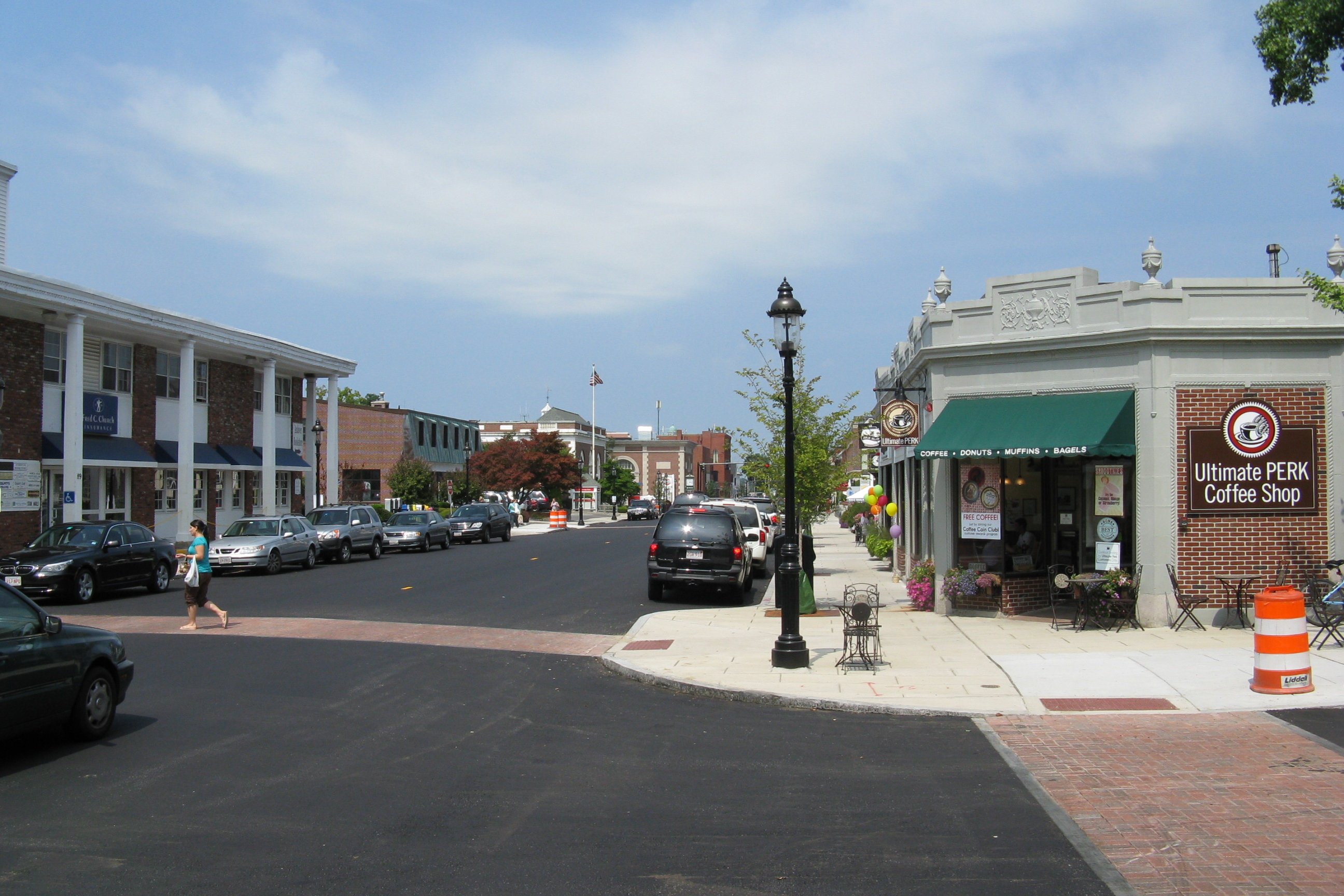 Storefronts and parked cars line a downtown street on a clear day.