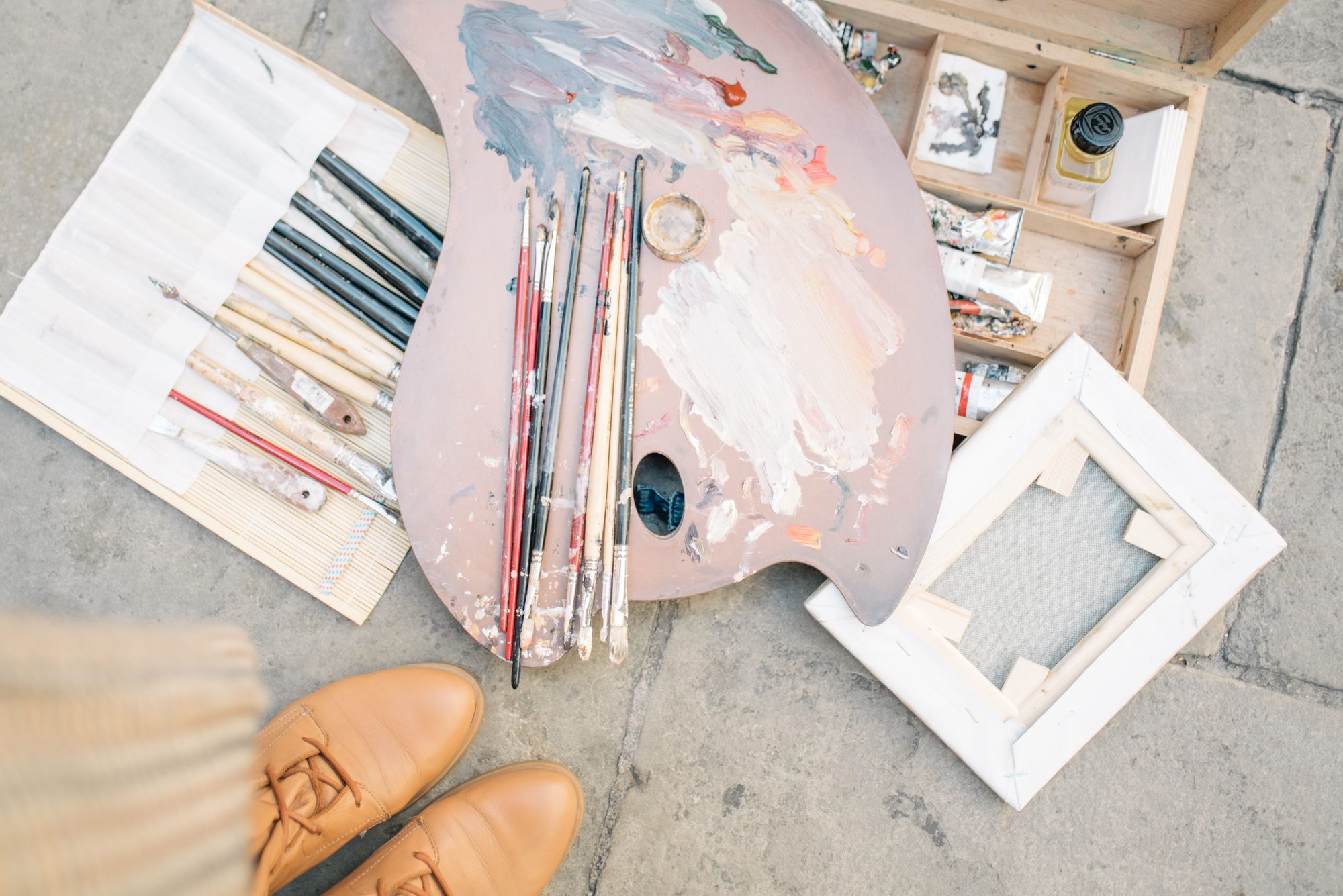 Aerial view of painting supplies and shoes on a concrete surface.
