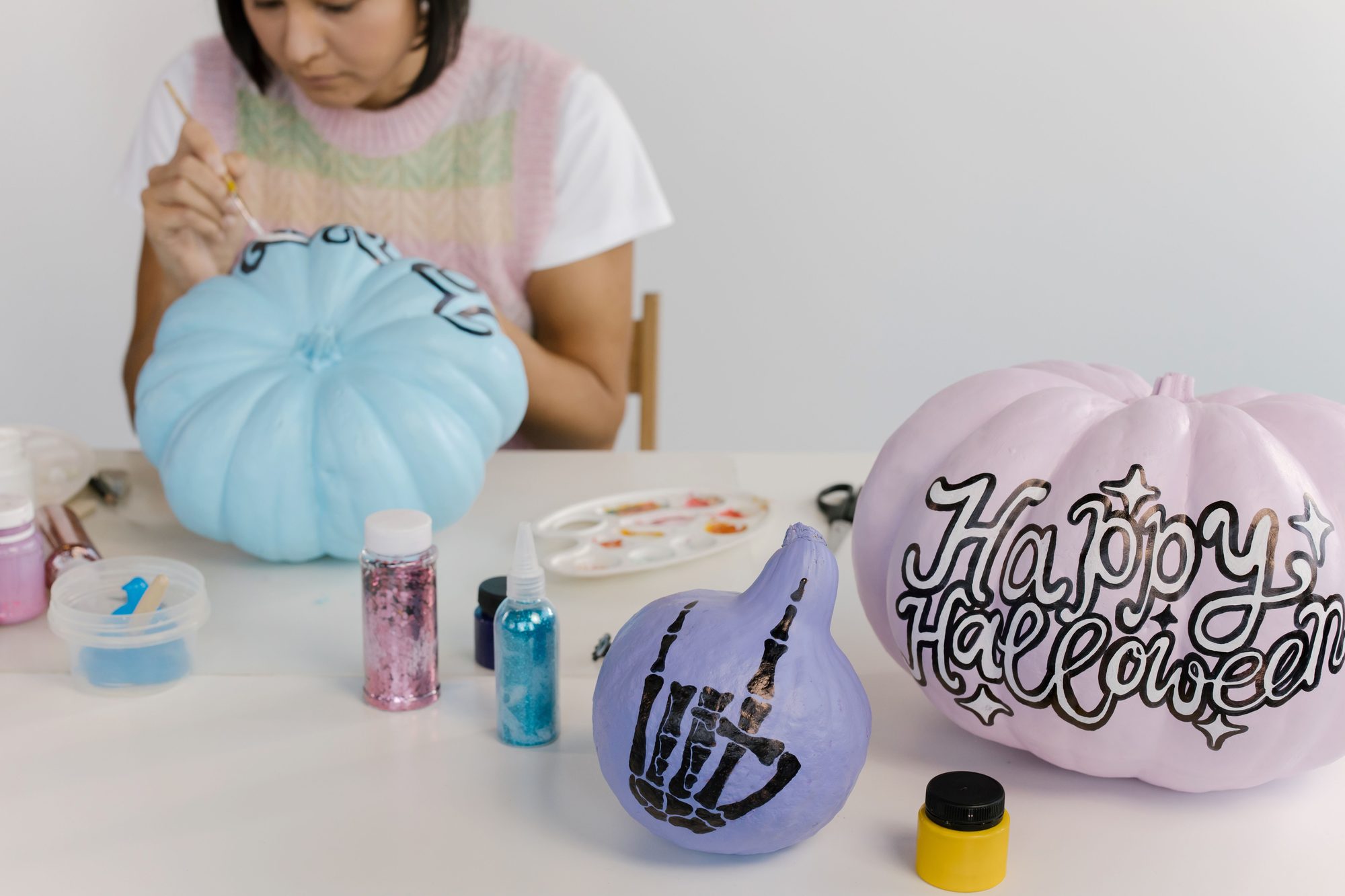 A person painting pastel Halloween pumpkins with designs and text at a crafting table.