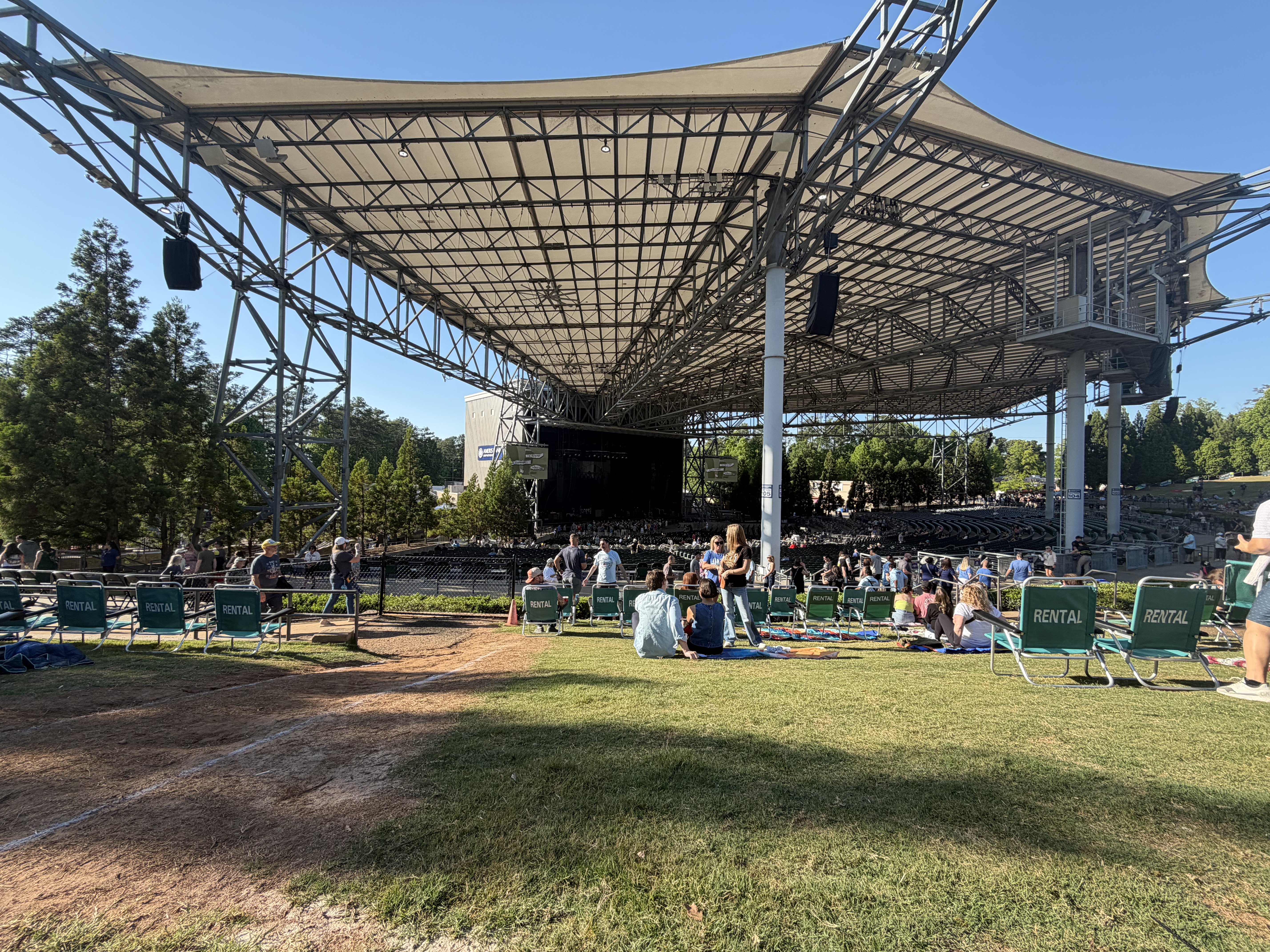 Open-air amphitheatre with a large steel canopy roof over the stage and green lawn seating.
