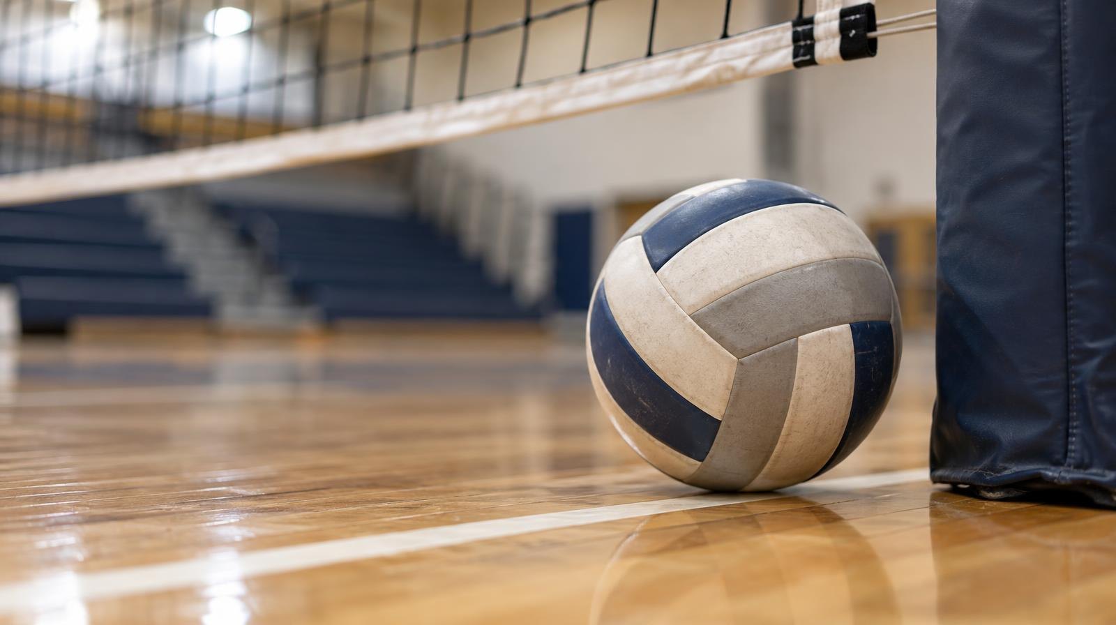 A volleyball resting on a gym floor next to a net post.
