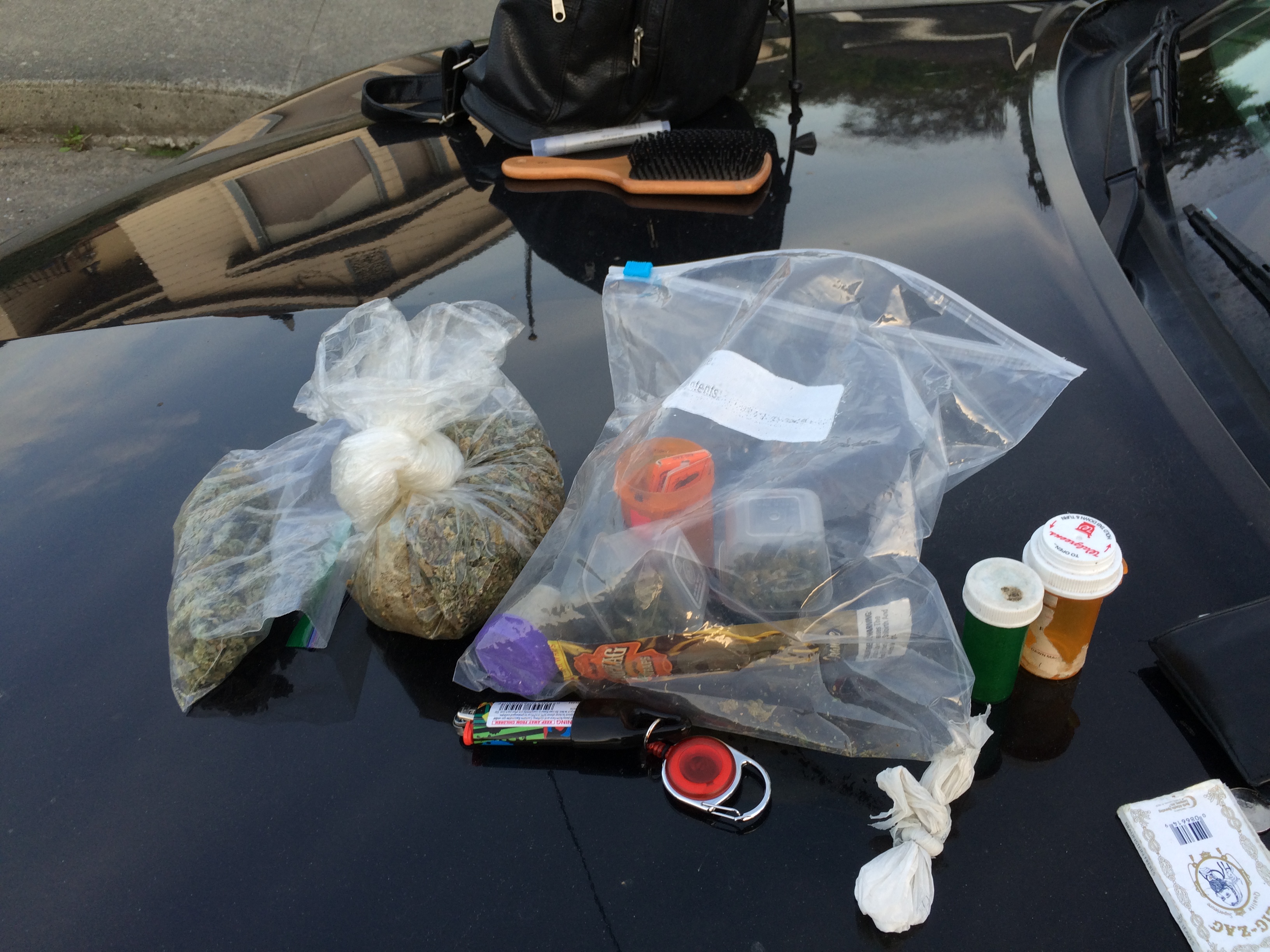 Seized drug bags, pill bottles, and paraphernalia displayed on the hood of a dark vehicle.