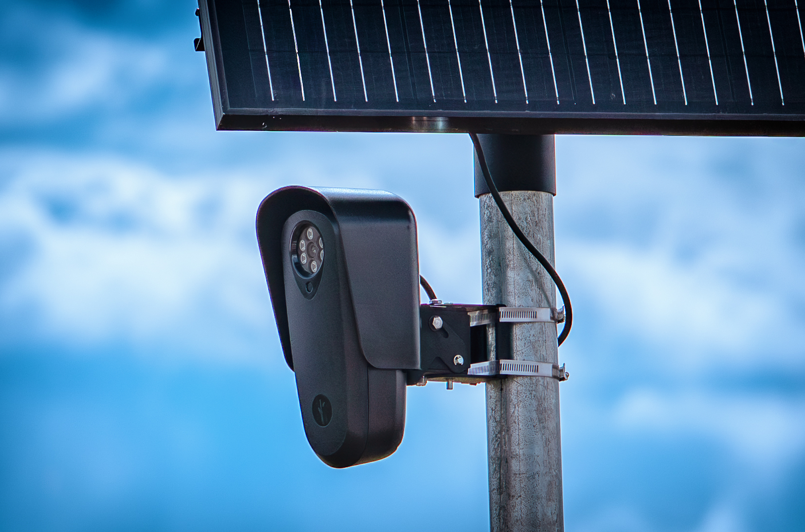 Close-up of a Flock Safety license plate reader camera on a pole under a blue sky.