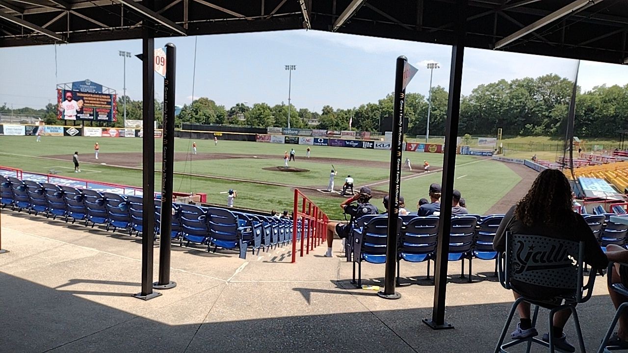 Baseball game underway at a minor league stadium with blue seats and a green outfield.