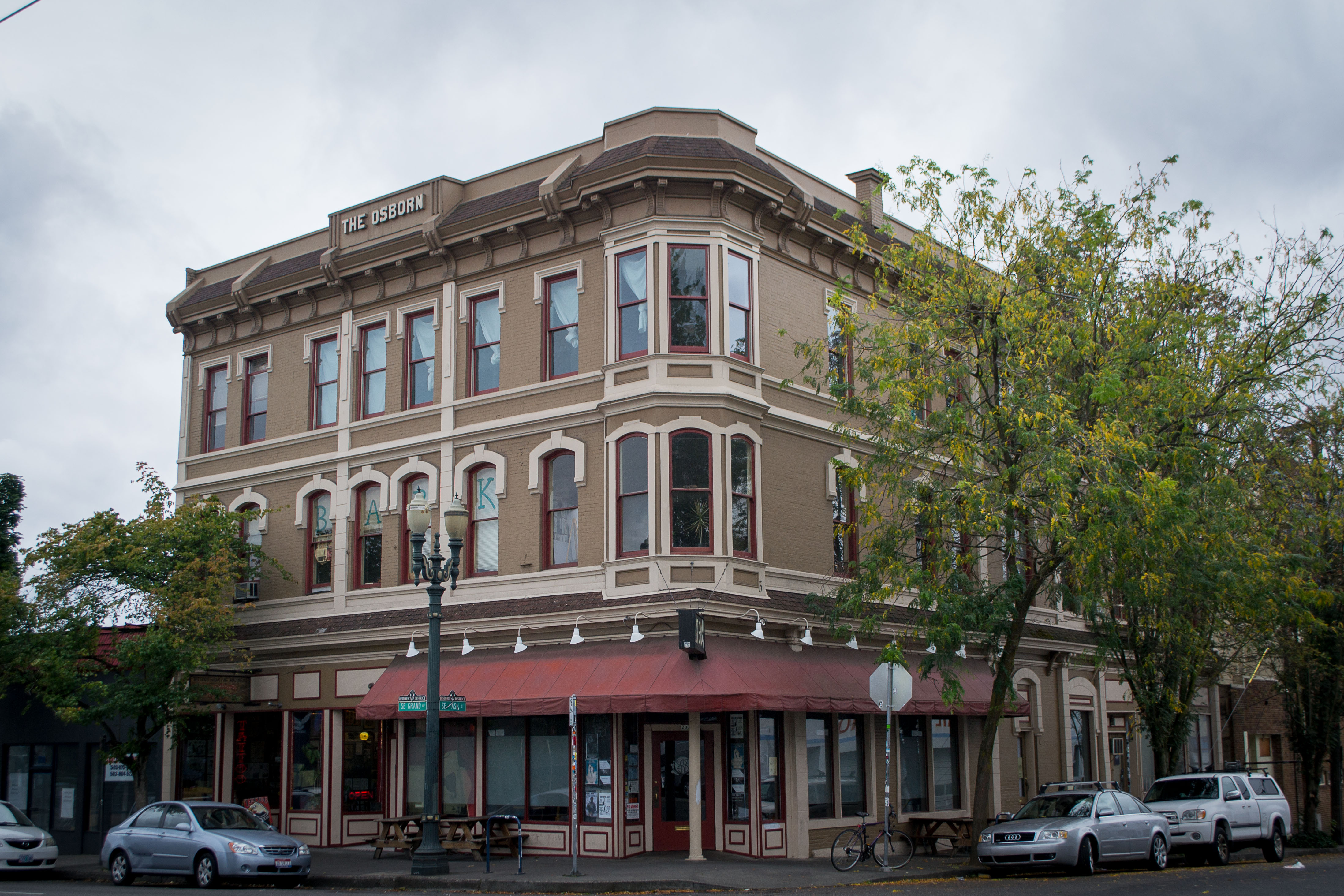 Three-story historic brick corner building with red awning and ornate Victorian details.