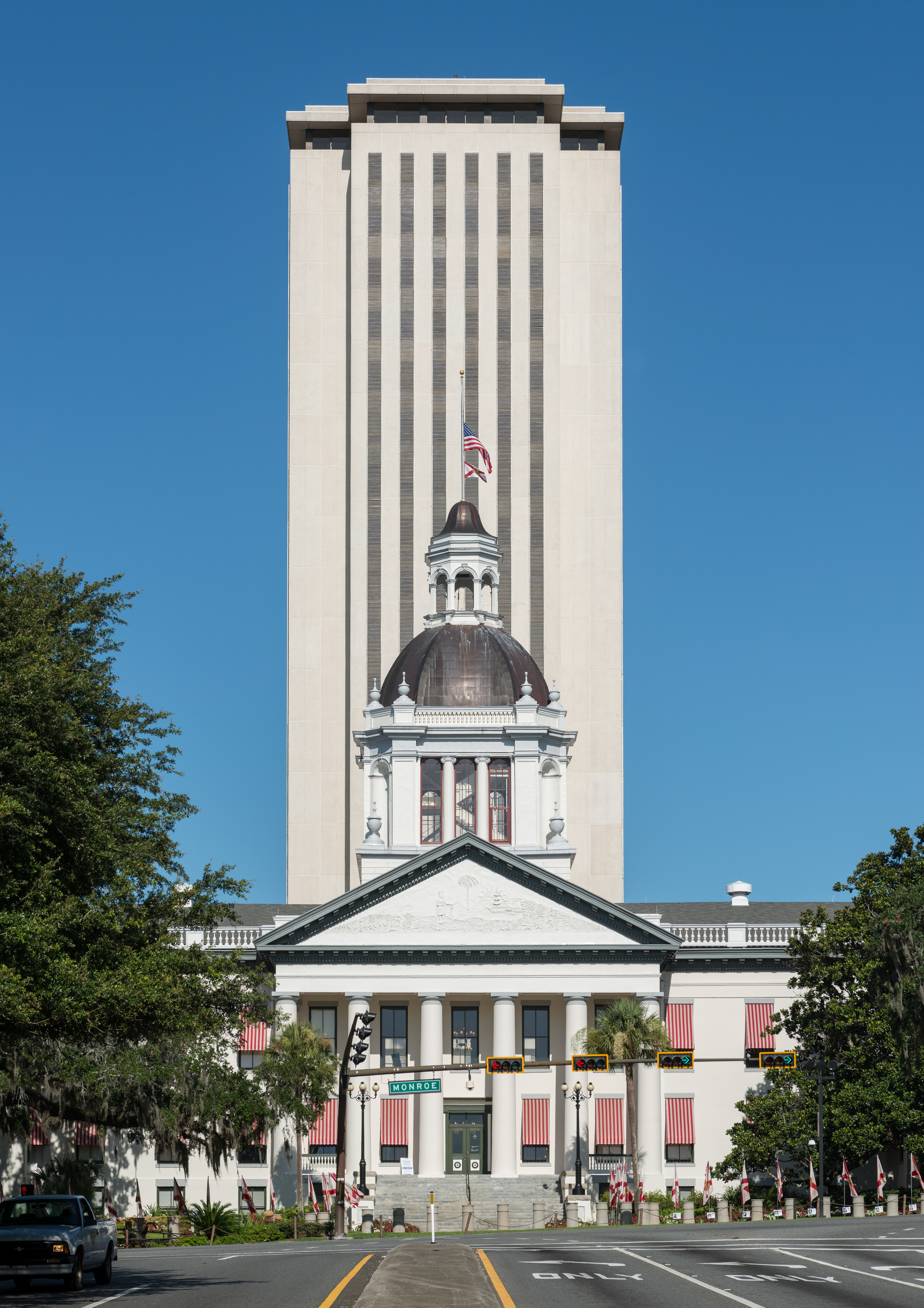 Historic domed capitol building with a modern high-rise tower behind it, framed by trees.