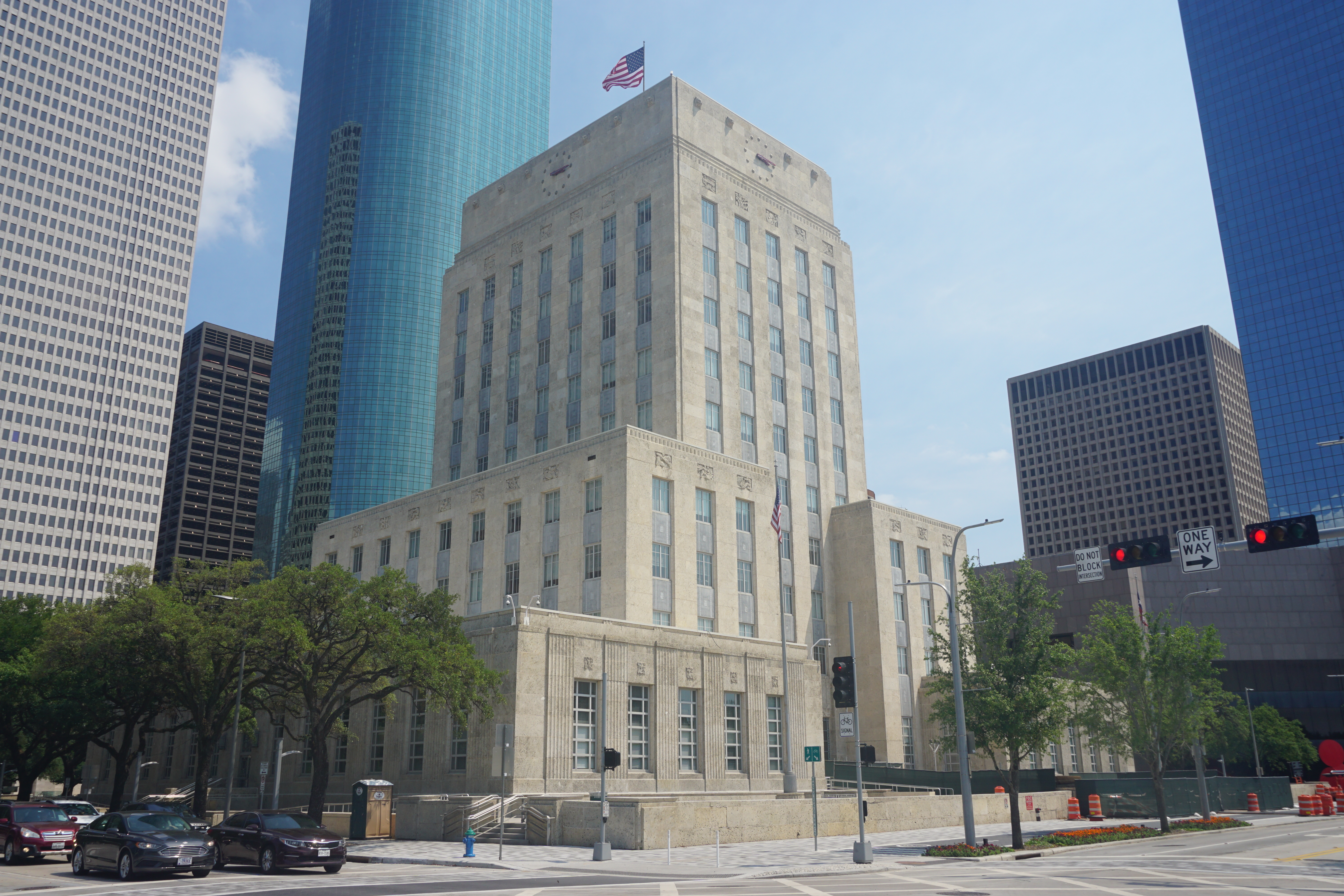 Multi-story Art Deco government building with an American flag on top, surrounded by glass skyscrapers.